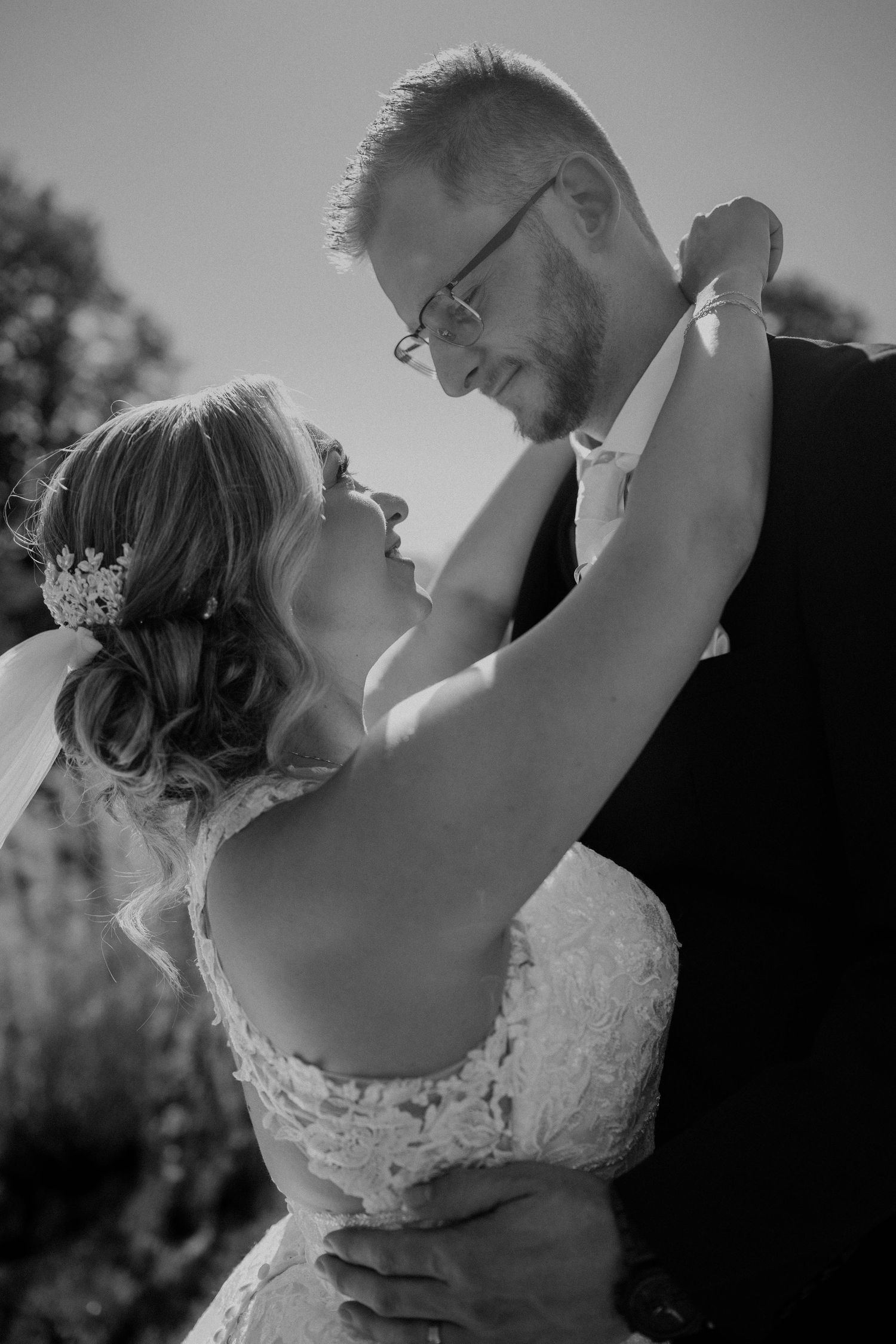 Black and white romantic portrait of bride and groom gazing at each other under sunny skies.