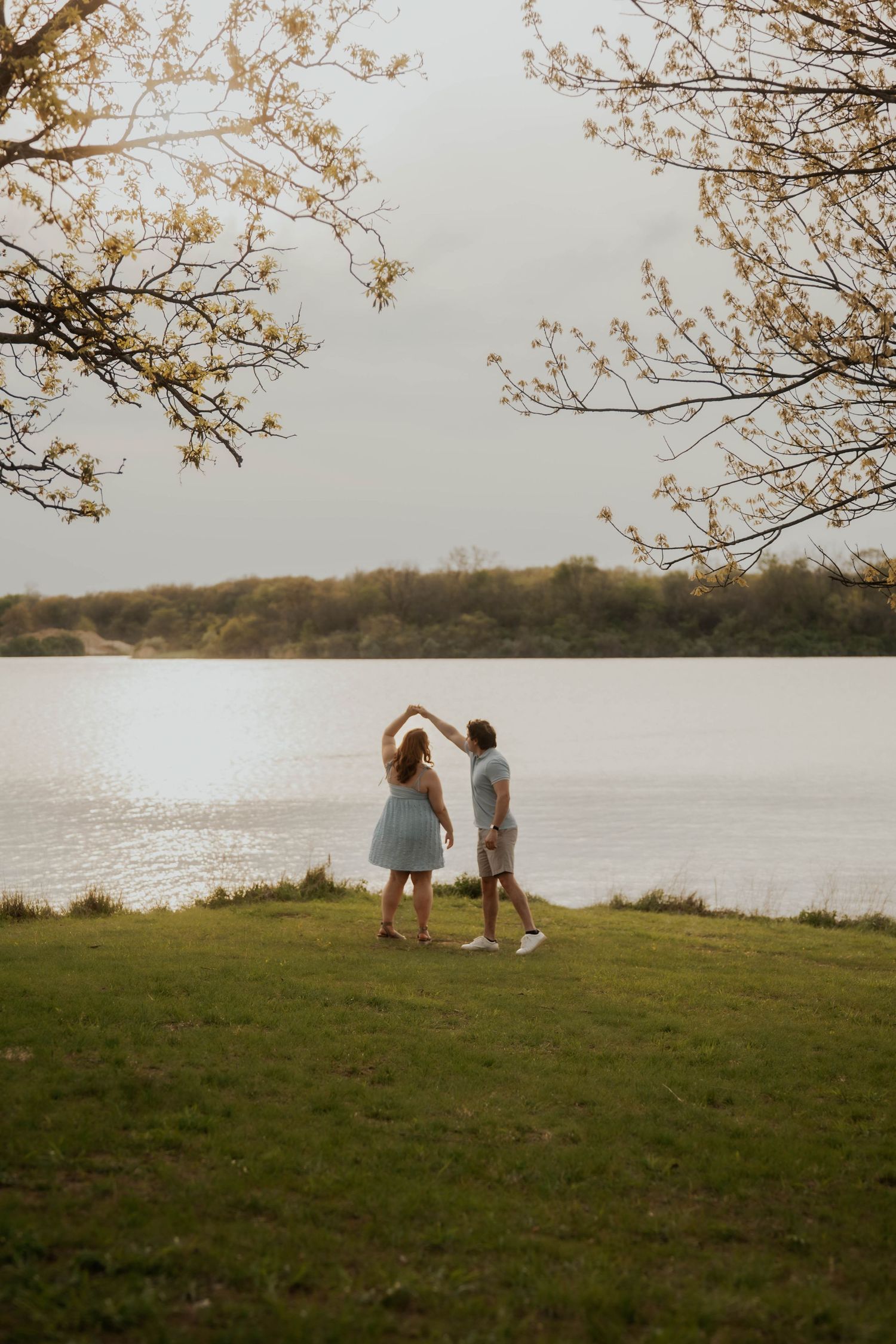 Couple dancing by a lake under blooming trees in spring.