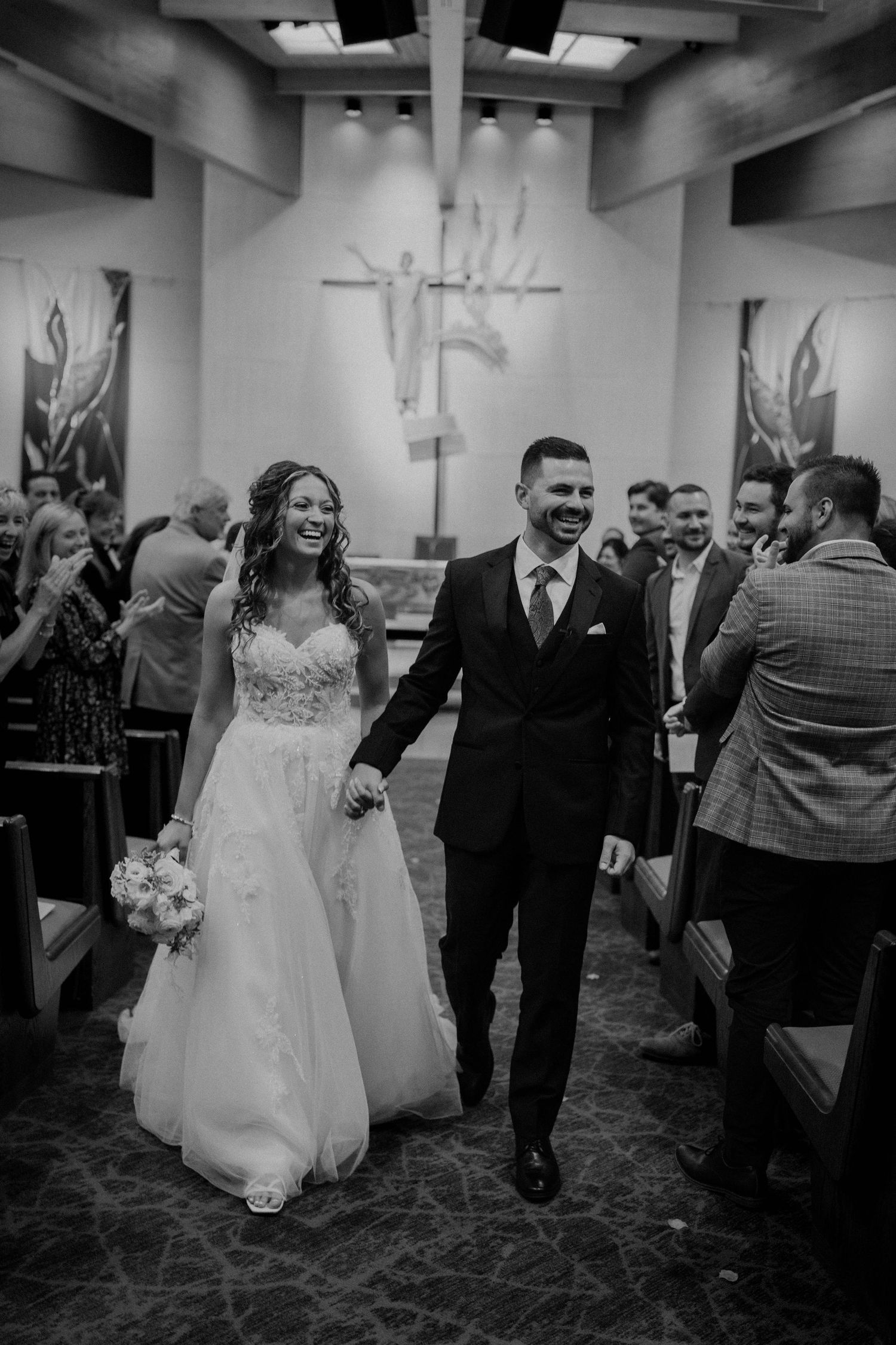 Joyful bride and groom walking down church aisle after wedding ceremony in black and white photo.