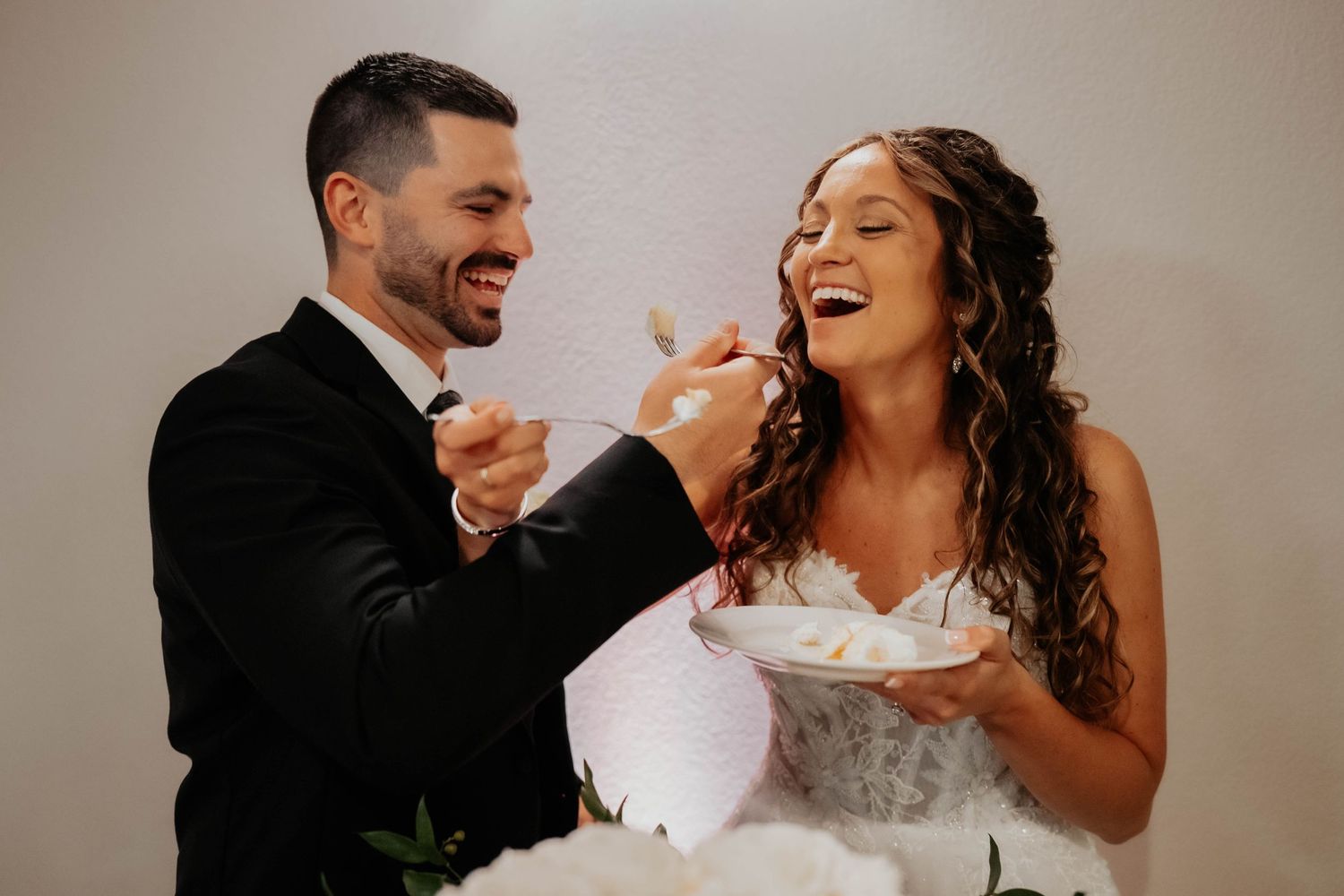 Joyful bride and groom sharing wedding cake during reception celebration.