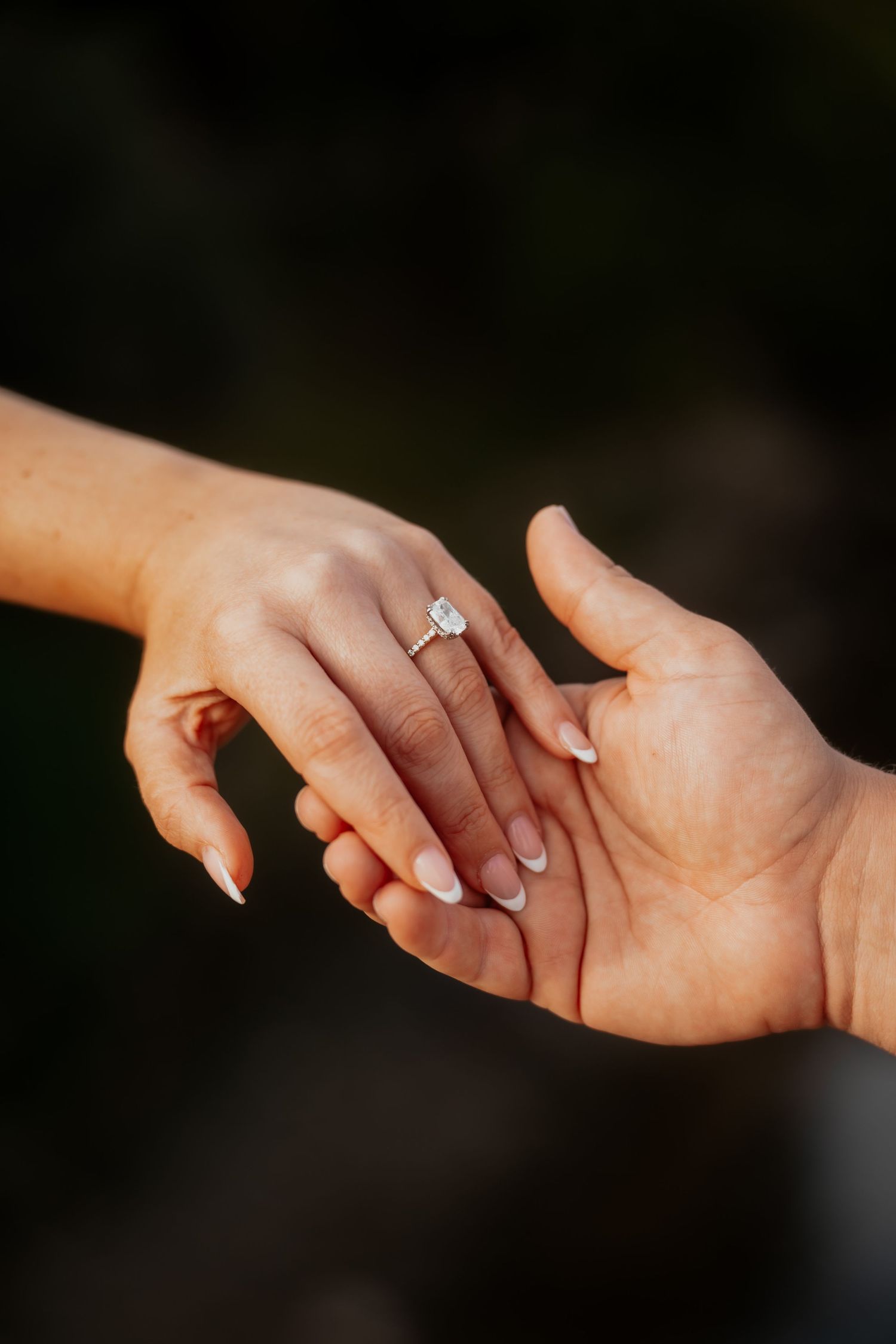 Close-up of an engagement ring on a woman's hand resting in a man's palm.