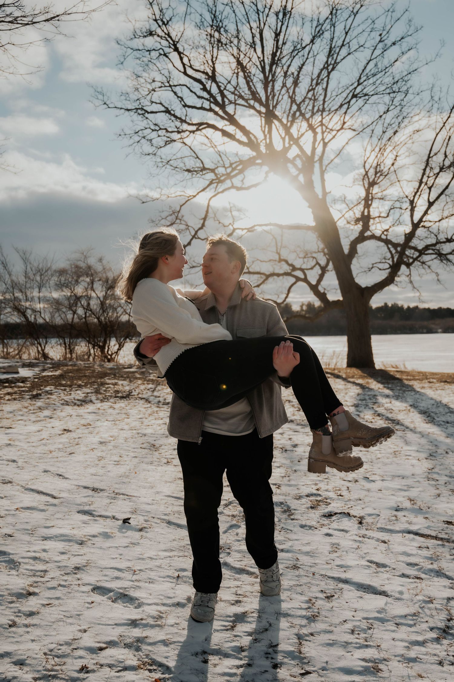 Man carrying woman in his arms on a snowy path with sunlight.