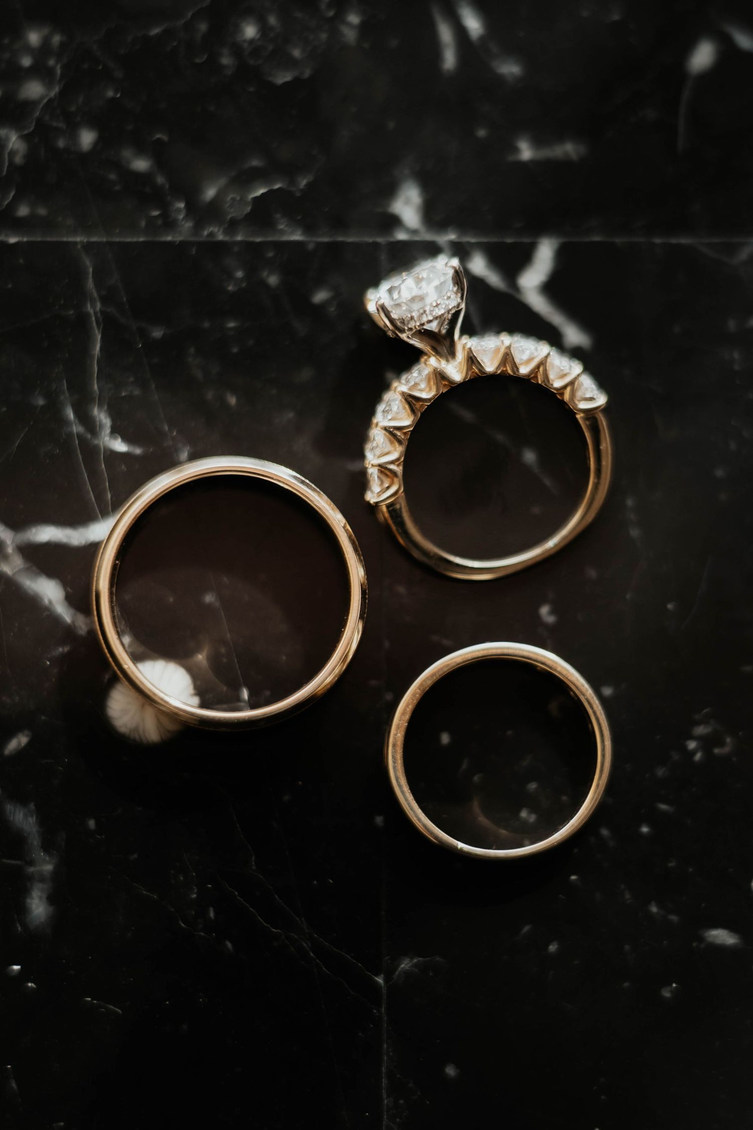 Three gold wedding rings and a diamond engagement ring displayed on a dark marble surface.