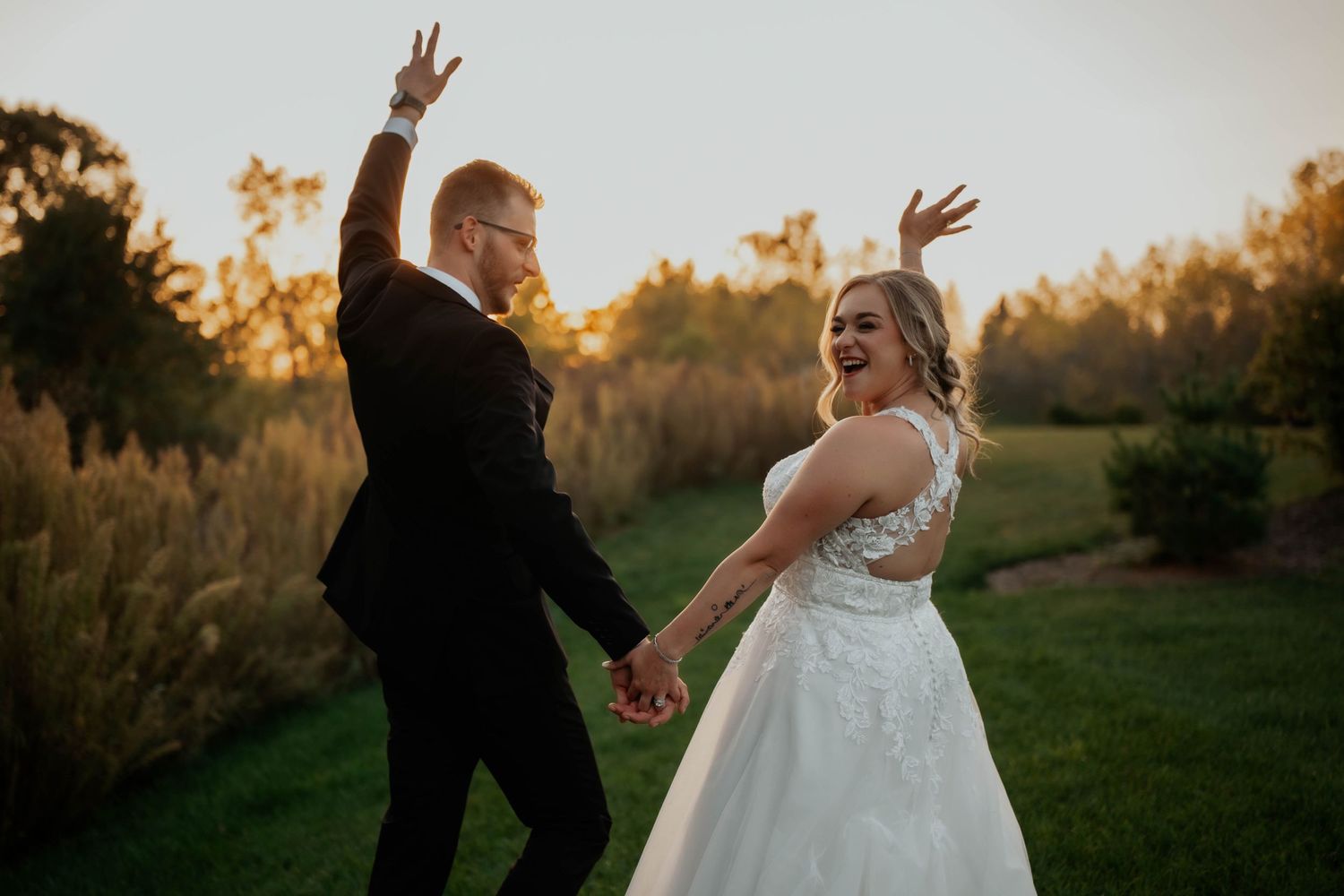 Joyful bride and groom laughing and celebrating outdoors at sunset during golden hour wedding photos.