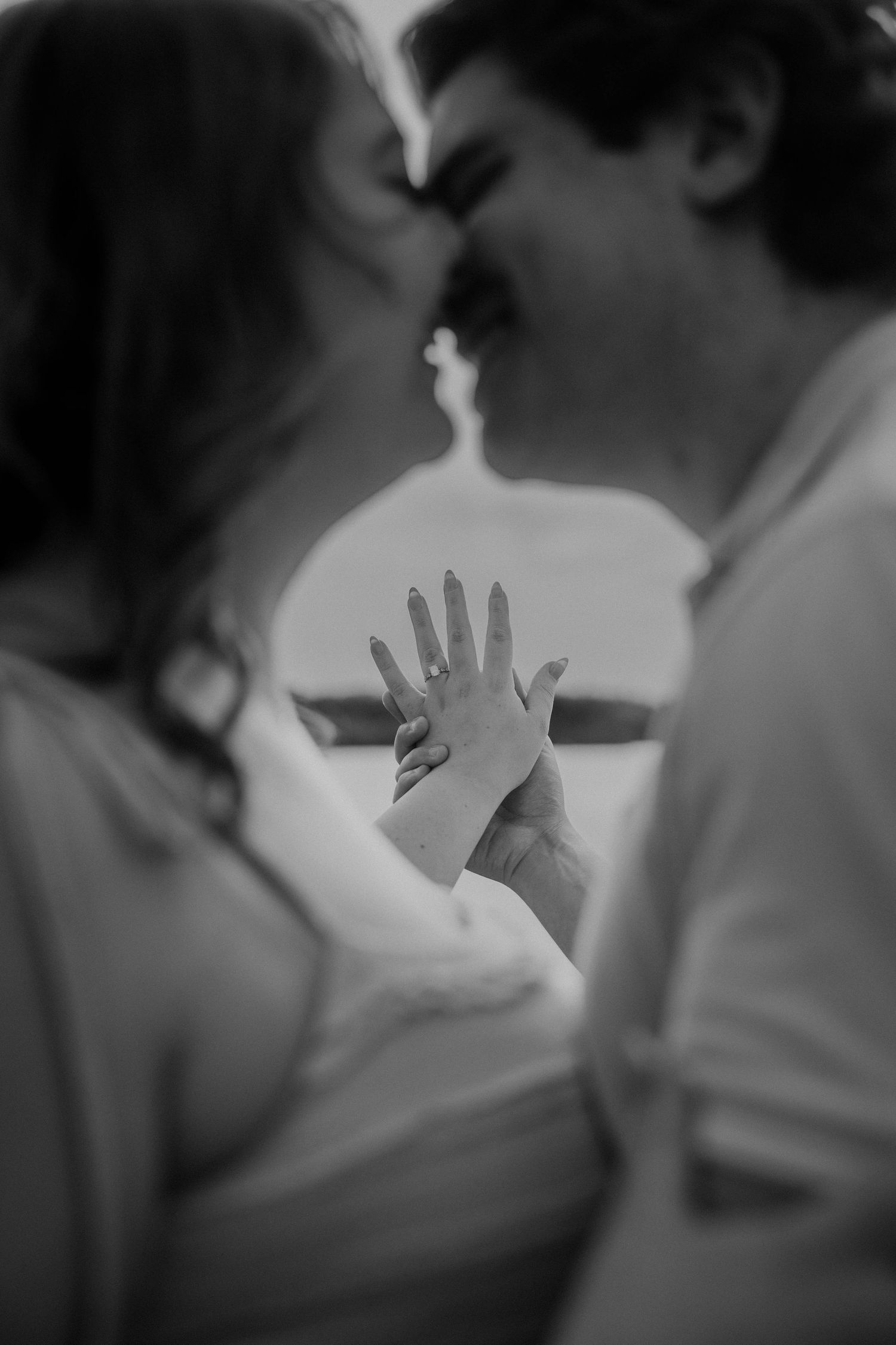 Black and white photo of couple kissing while showing engagement ring.