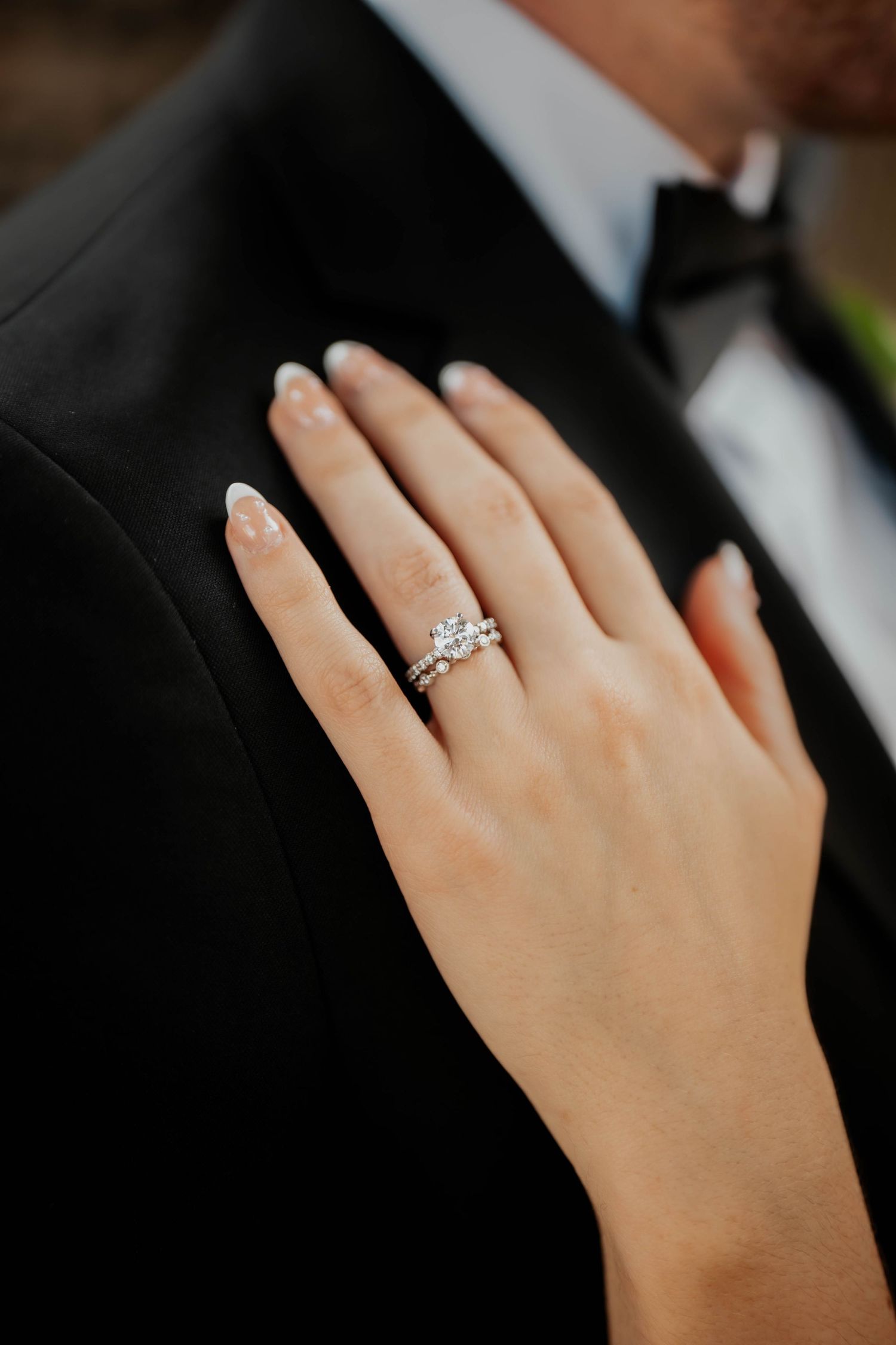 Close-up of bride's diamond engagement ring and wedding band on groom's lapel.