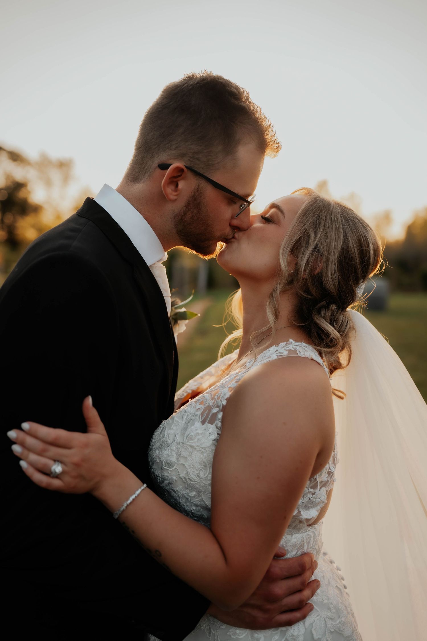 Bride and groom sharing a romantic kiss at golden hour, bride wearing lace wedding gown and veil.