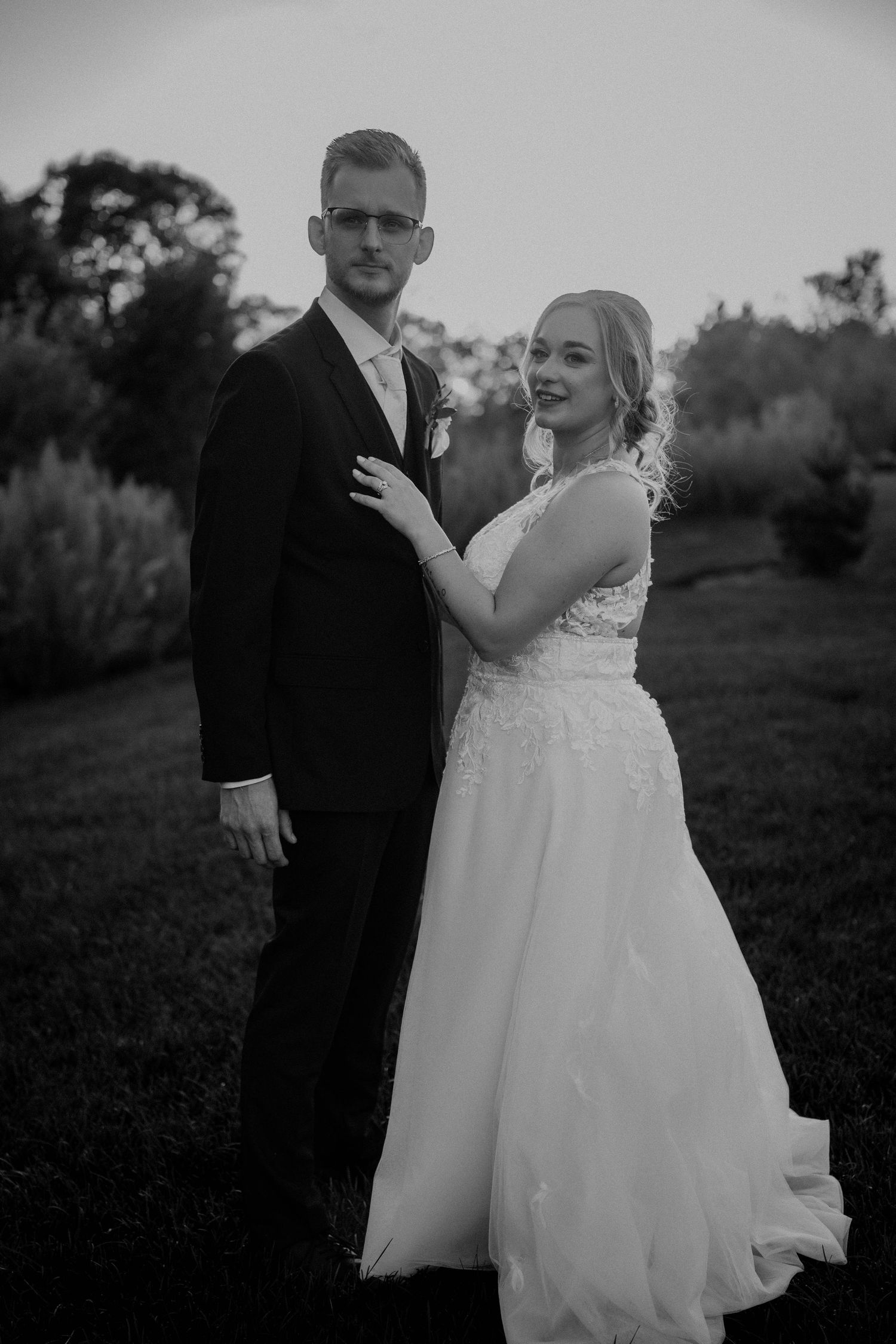 Classic black and white portrait of bride and groom posing together in garden at twilight.