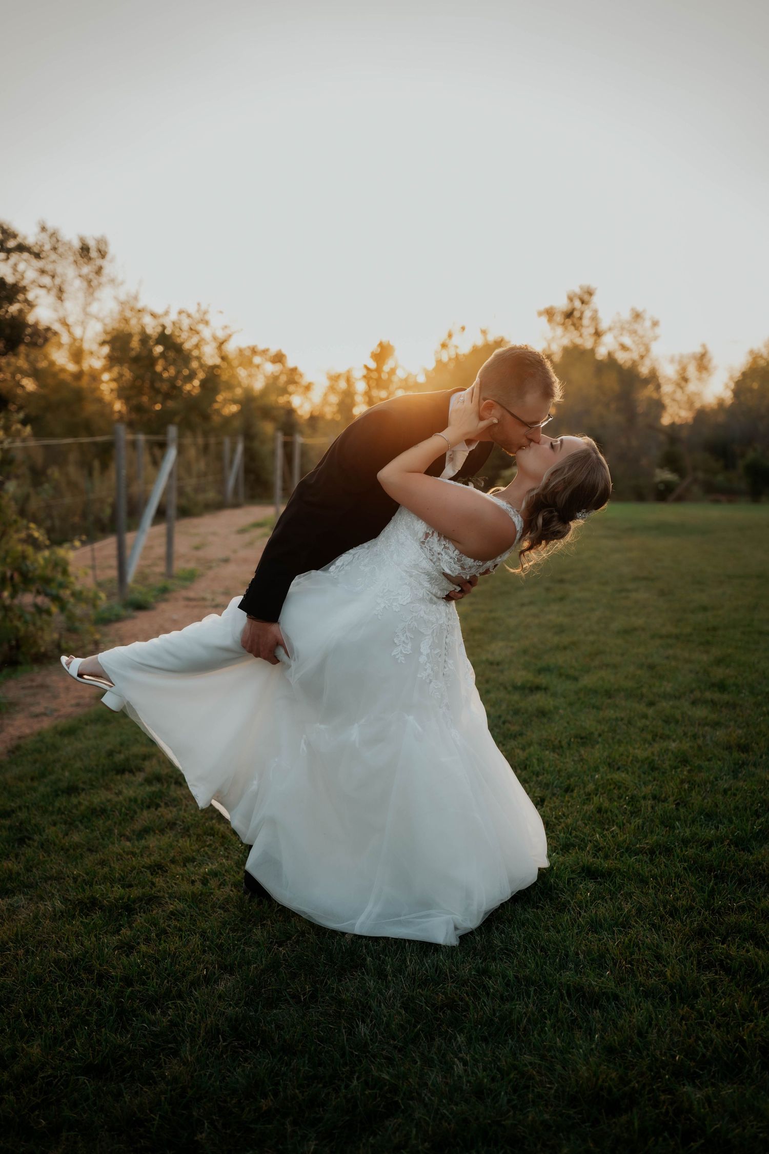 Groom dipping bride in elegant white wedding dress for a romantic kiss during golden hour sunset.