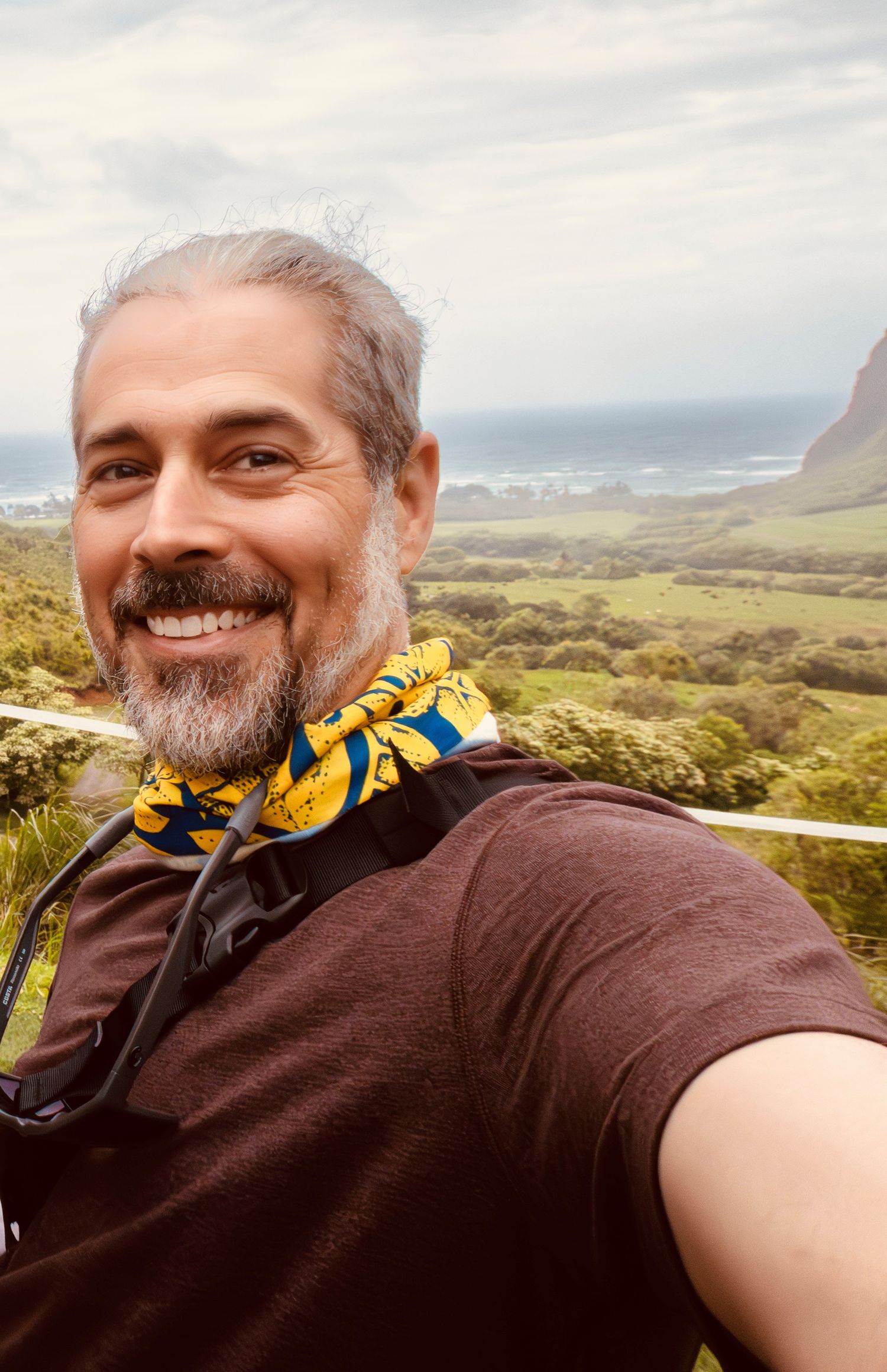Adventure selfies showing scenic mountain and coastal views while wearing brown shirt and patterned bandana.