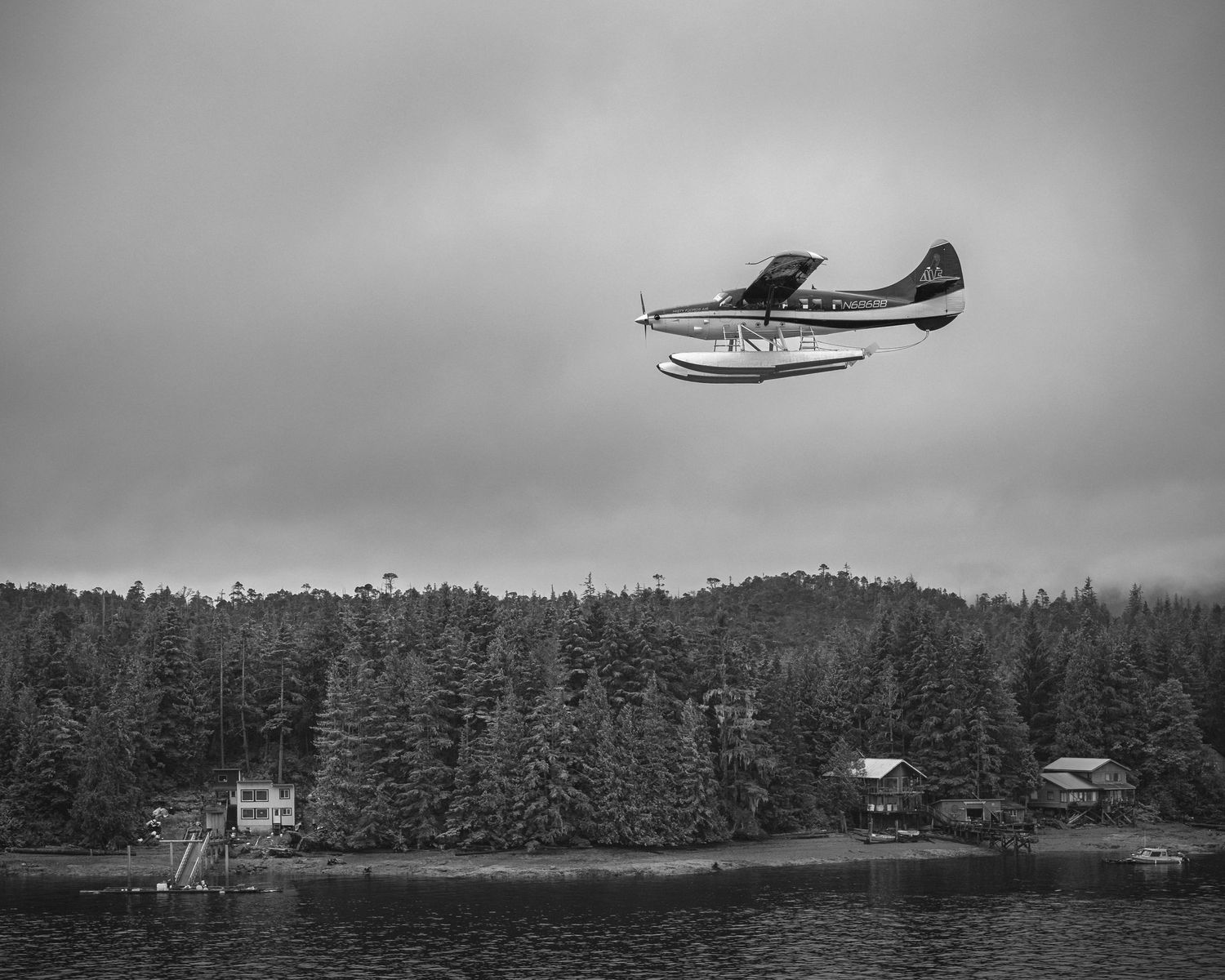 Seaplanes flying low over forested coastline in black and white photograph.