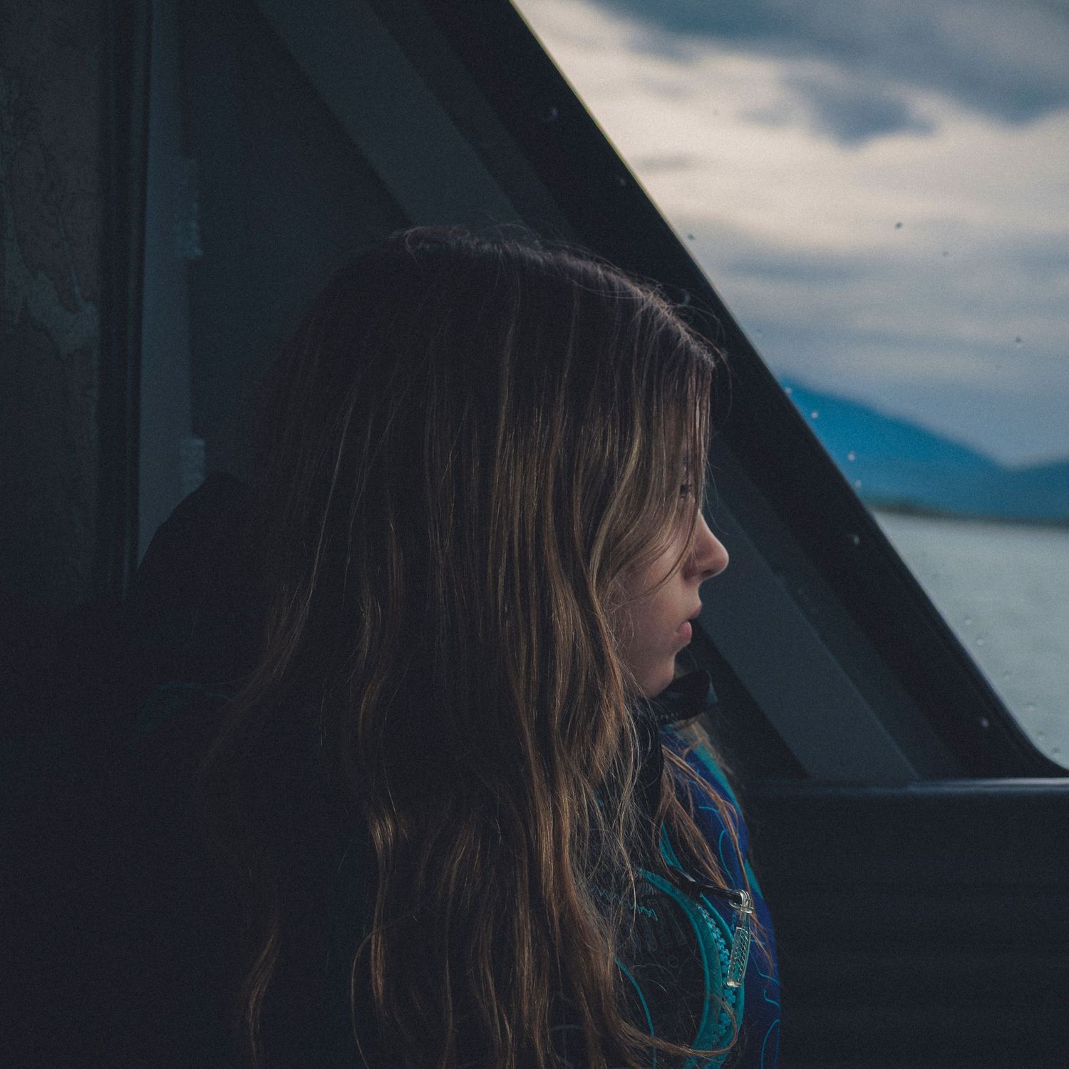 Person gazing out window with mountains and cloudy sky visible in background.