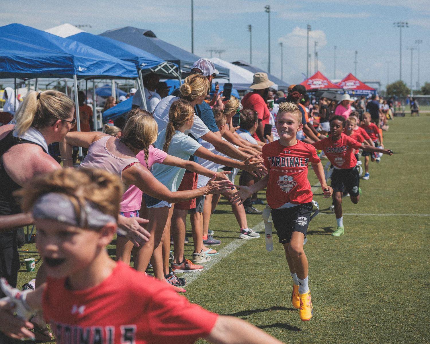 Athletes stretching in rows on outdoor field under blue pop-up tents.