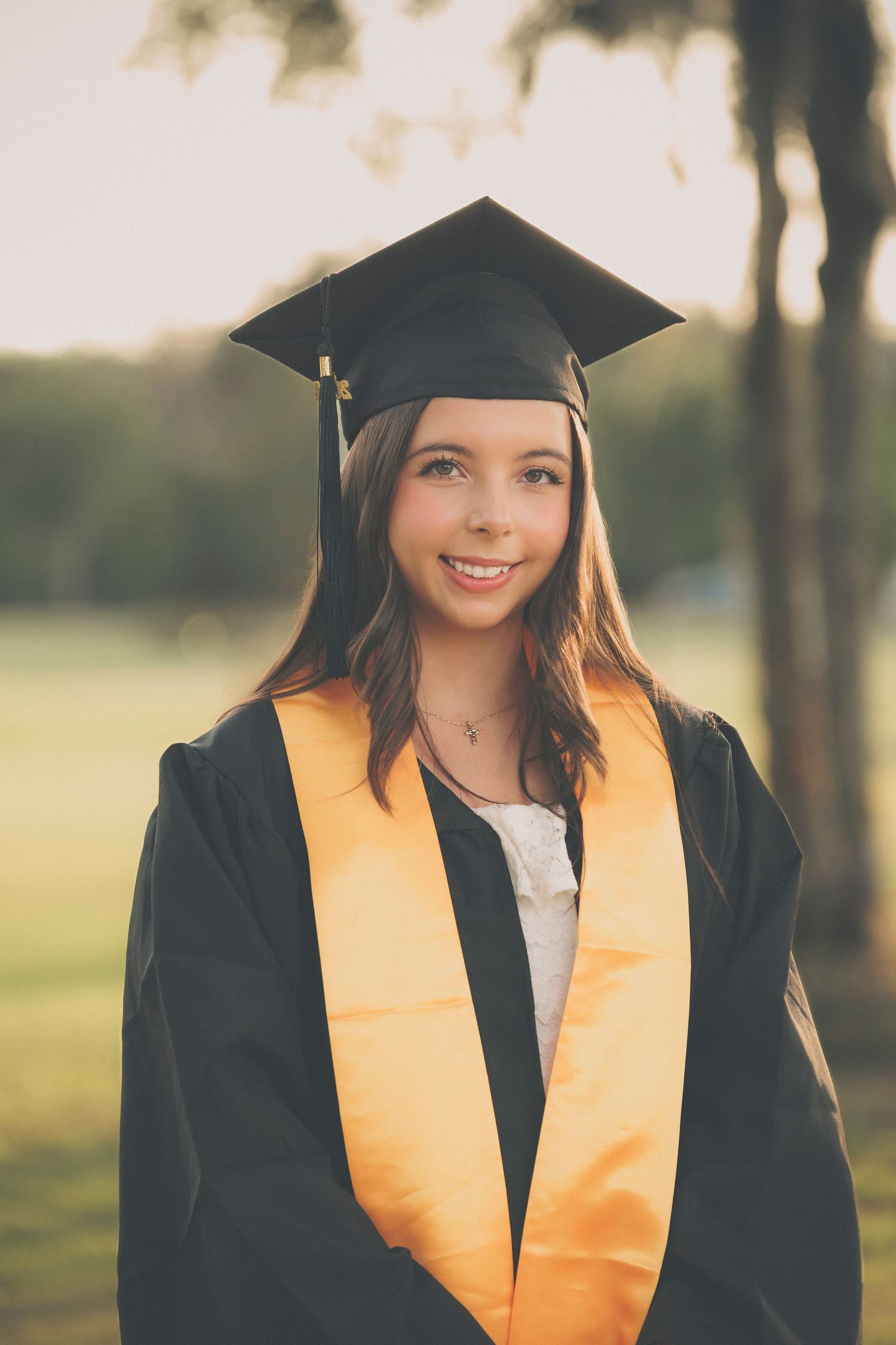 Graduate wearing gold honors stole and black cap poses for outdoor portraits.