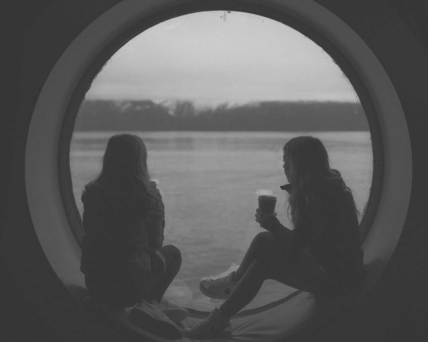 Silhouettes of observers looking through round windows at water view.