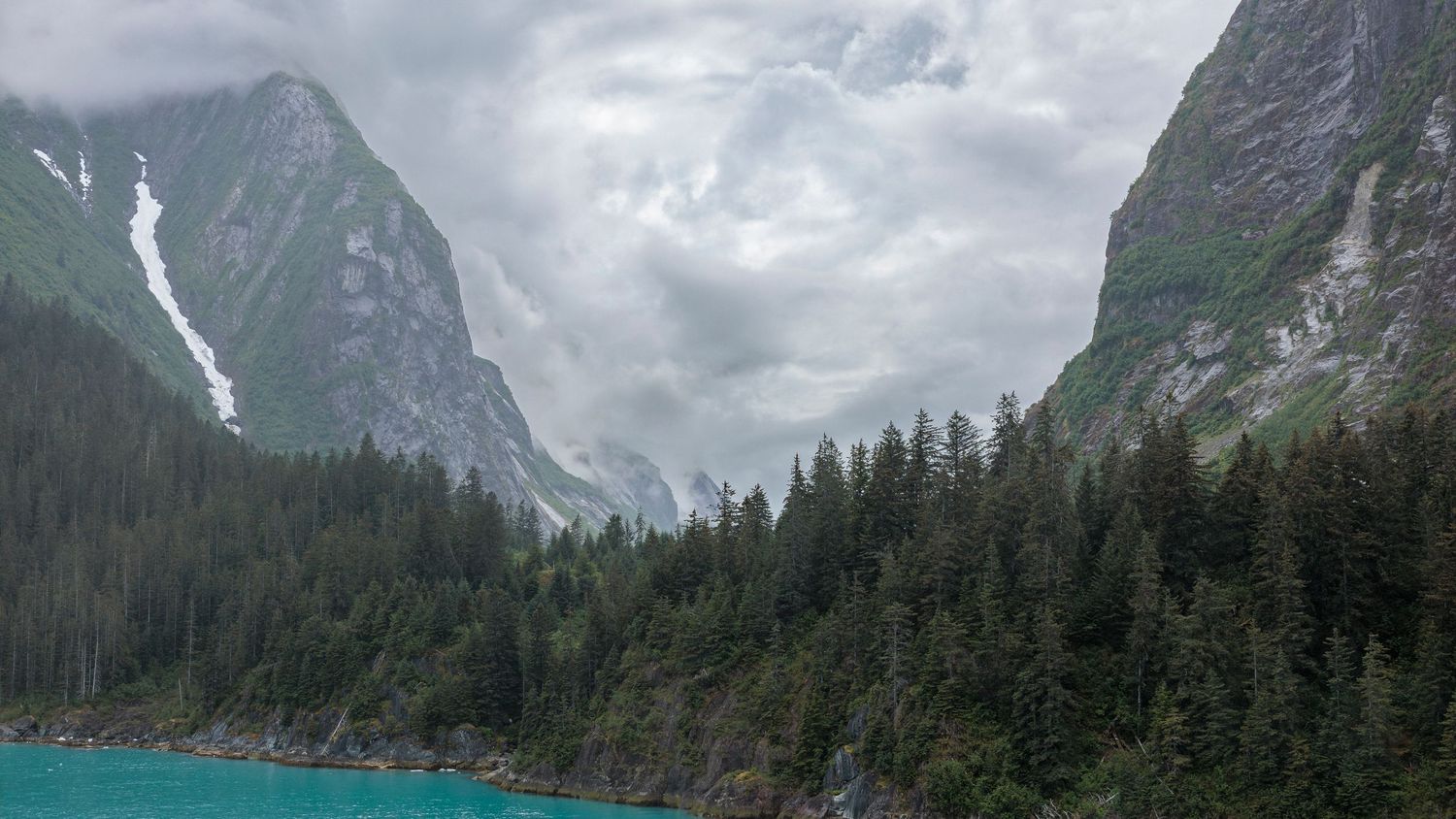Panoramic view of steep mountain cliffs rising from glacial waters in Alaska.