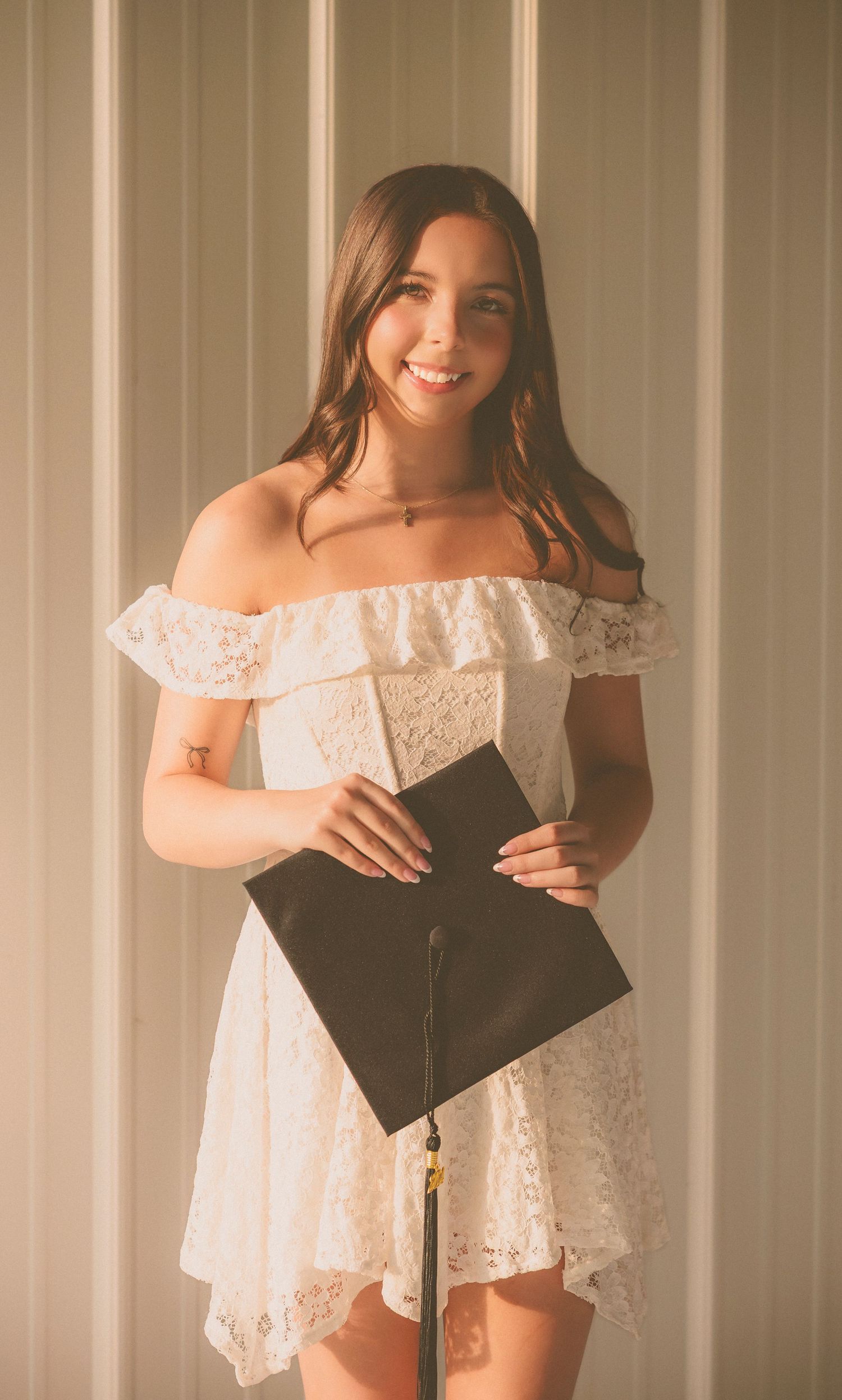 Graduate photography session holding a black cap against white paneling background.