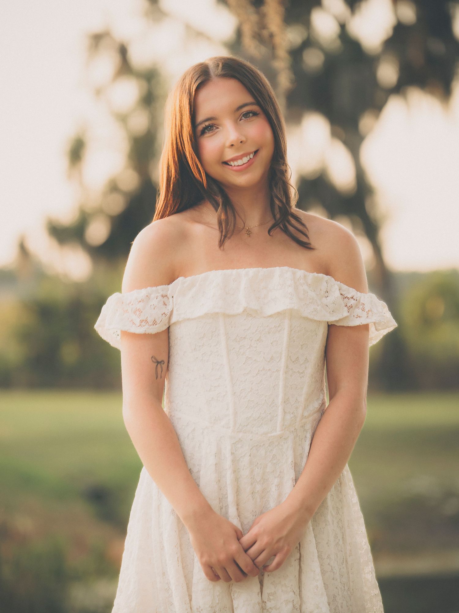 Senior portrait session featuring white off-shoulder lace dress in outdoor natural setting.