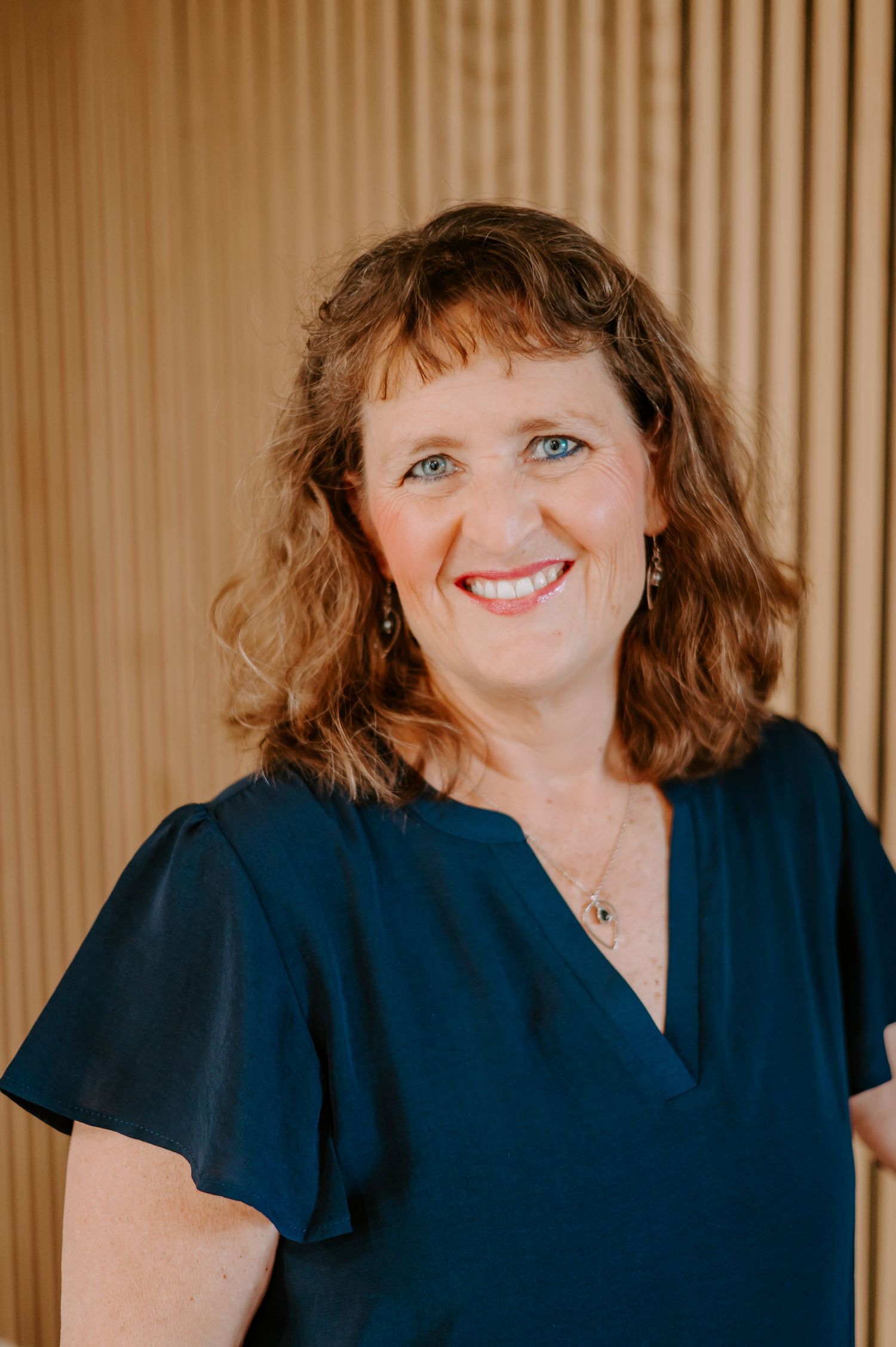 Person in navy blue v-neck top smiling against wood paneled background.
