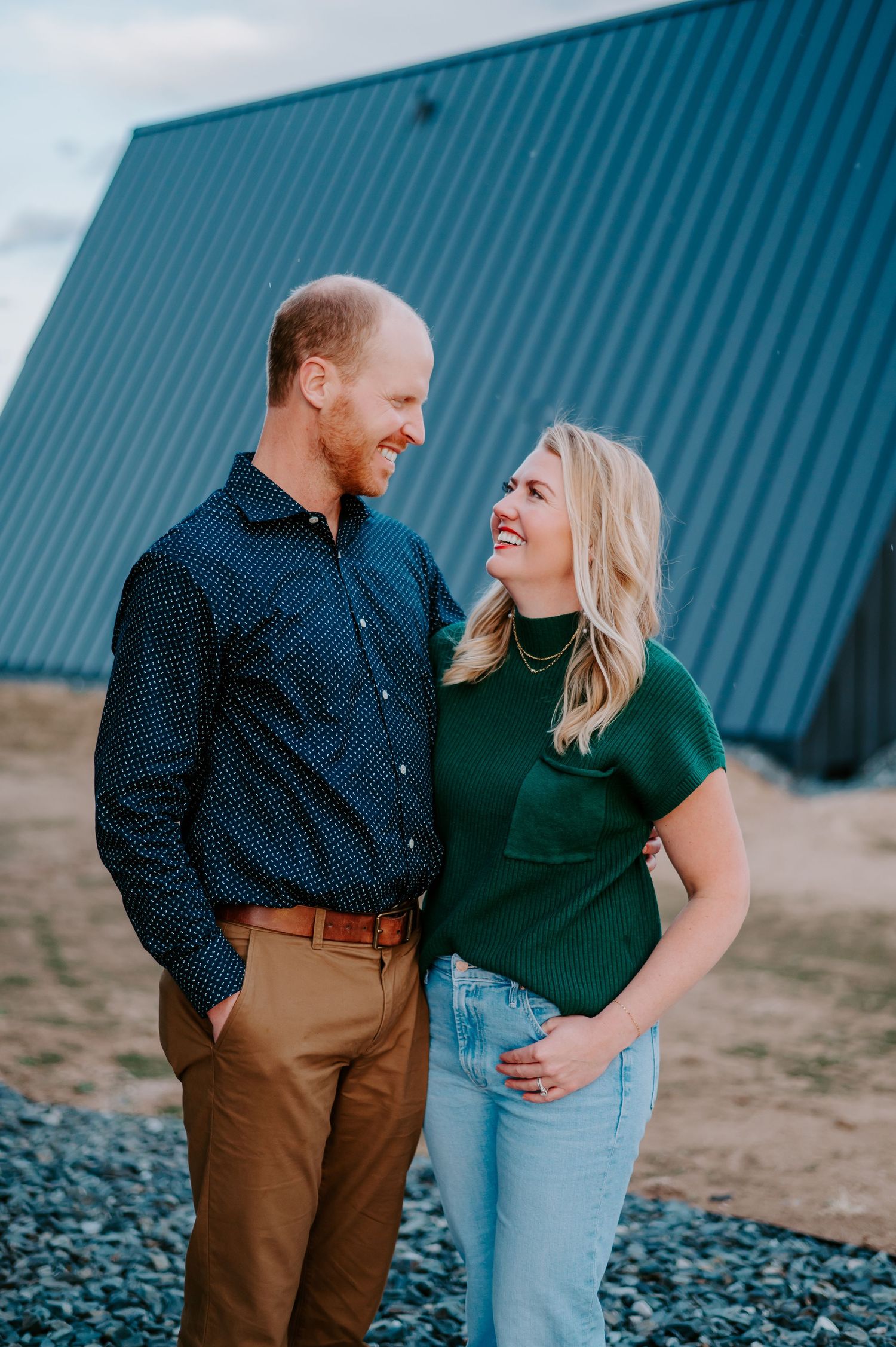 Couple in casual outfits sharing a laugh against blue metal building exterior.