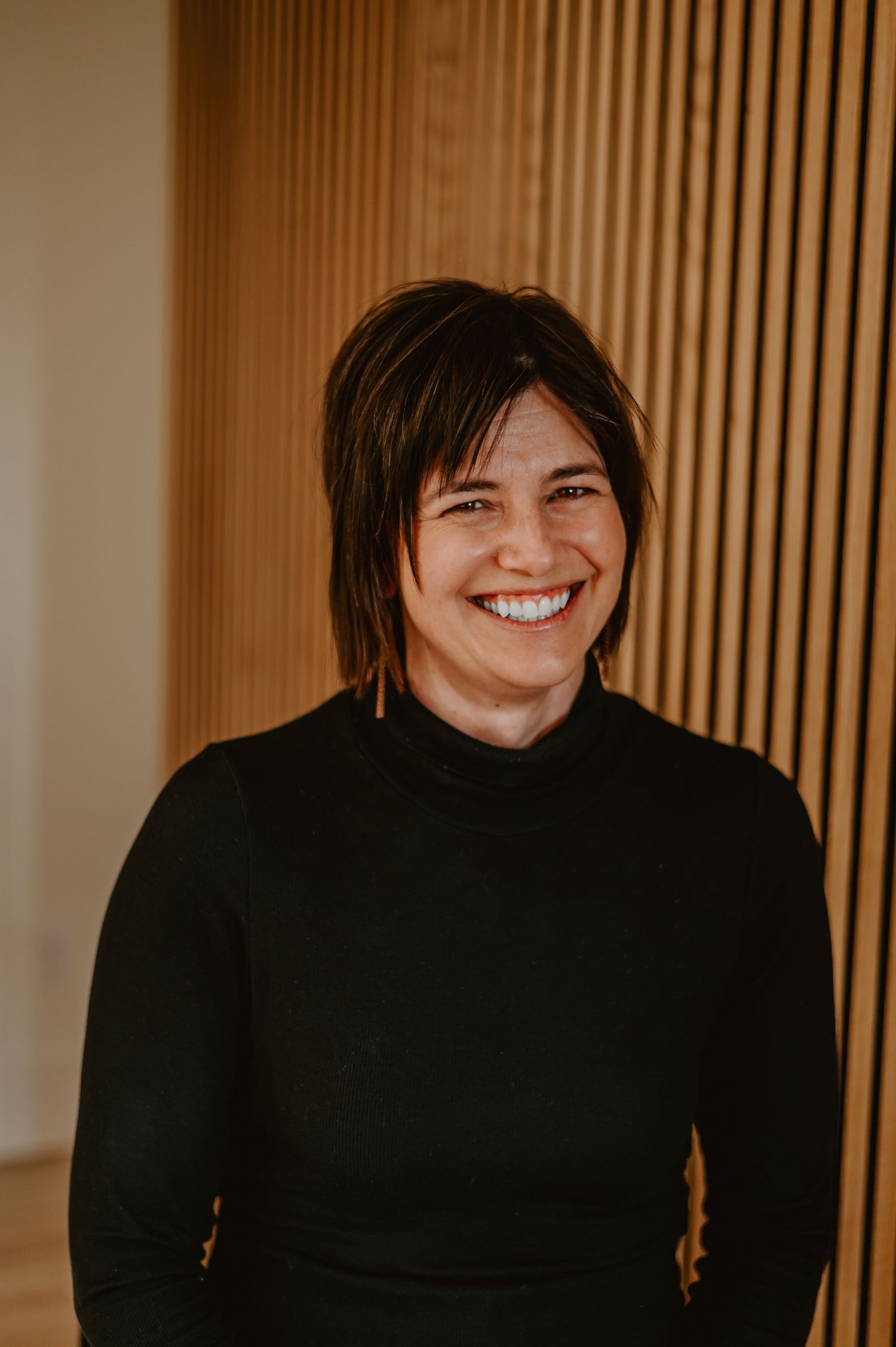 Portrait series showing someone in black sweater smiling against wooden slat background.