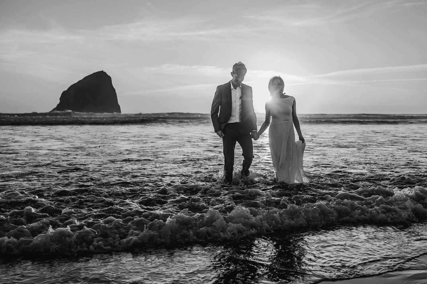 Black and white coastal landscape with silhouettes walking along rocky shoreline at sunset.