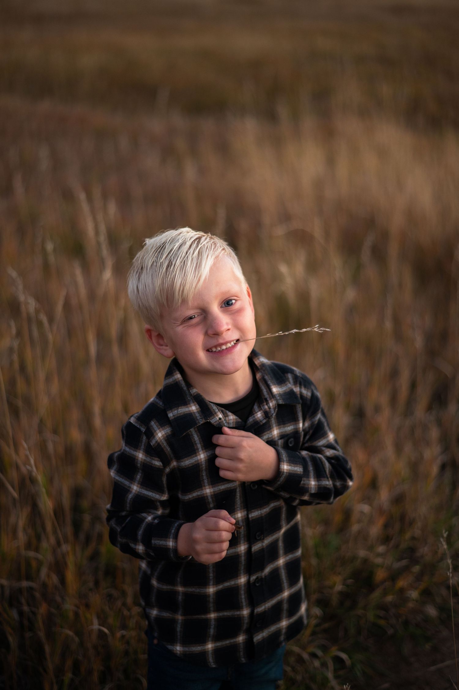 A child being silly standing outdoors in a hay field with grass in his mouth