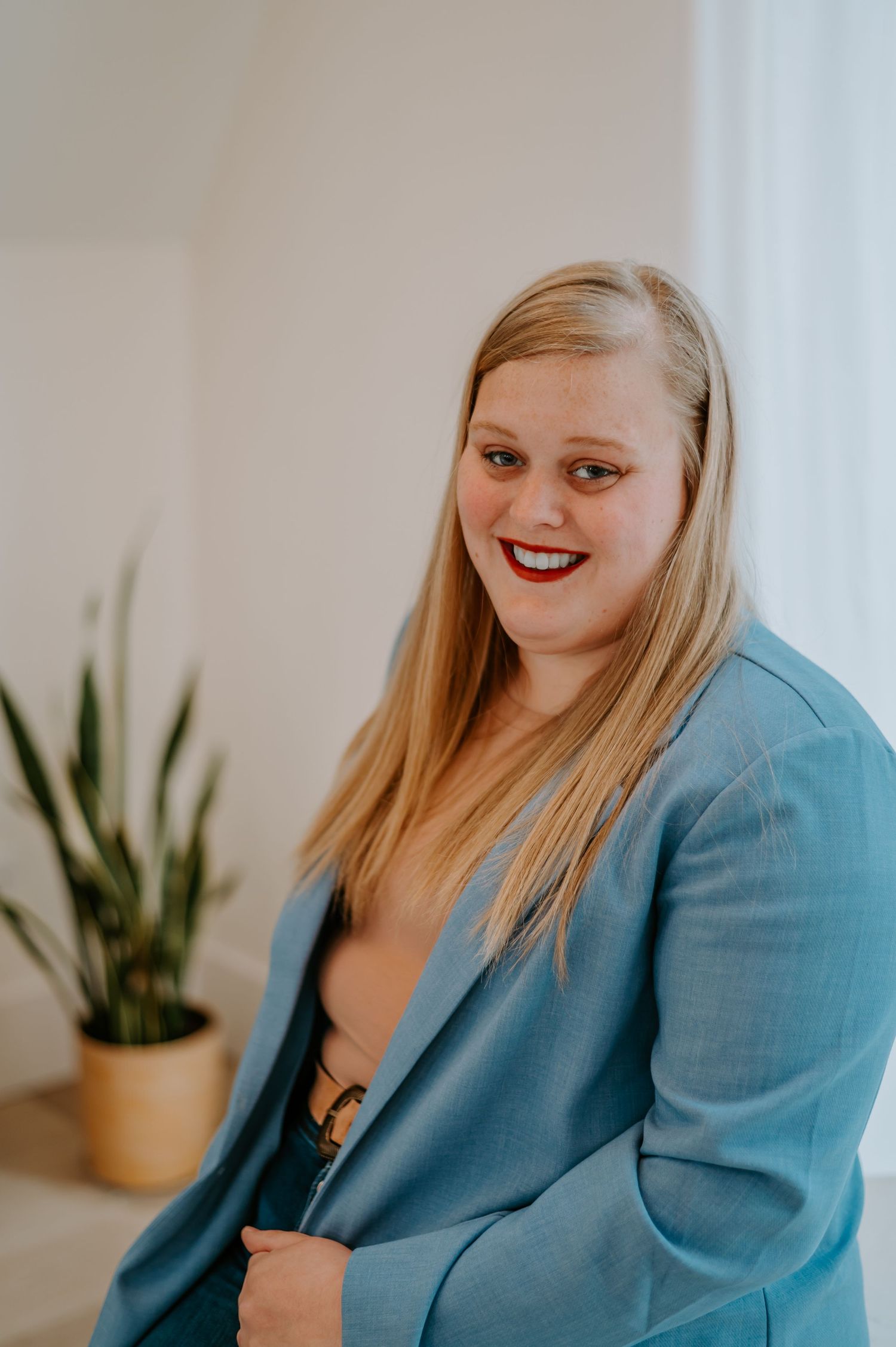 Indoor portrait featuring a light blue blazer and casual attire against a white wall with plants.