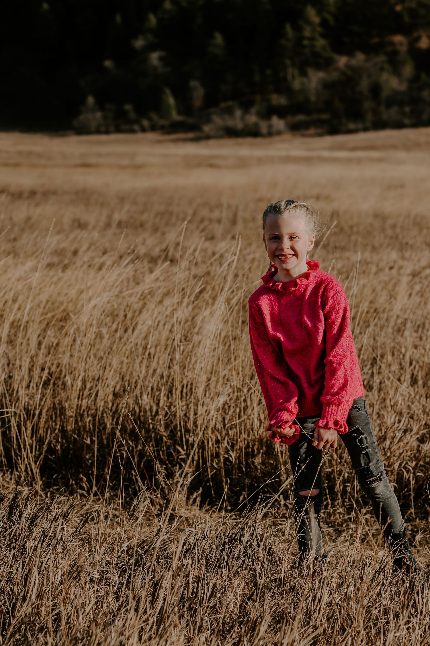 Child in red sweater playing in golden autumn field during sunset.