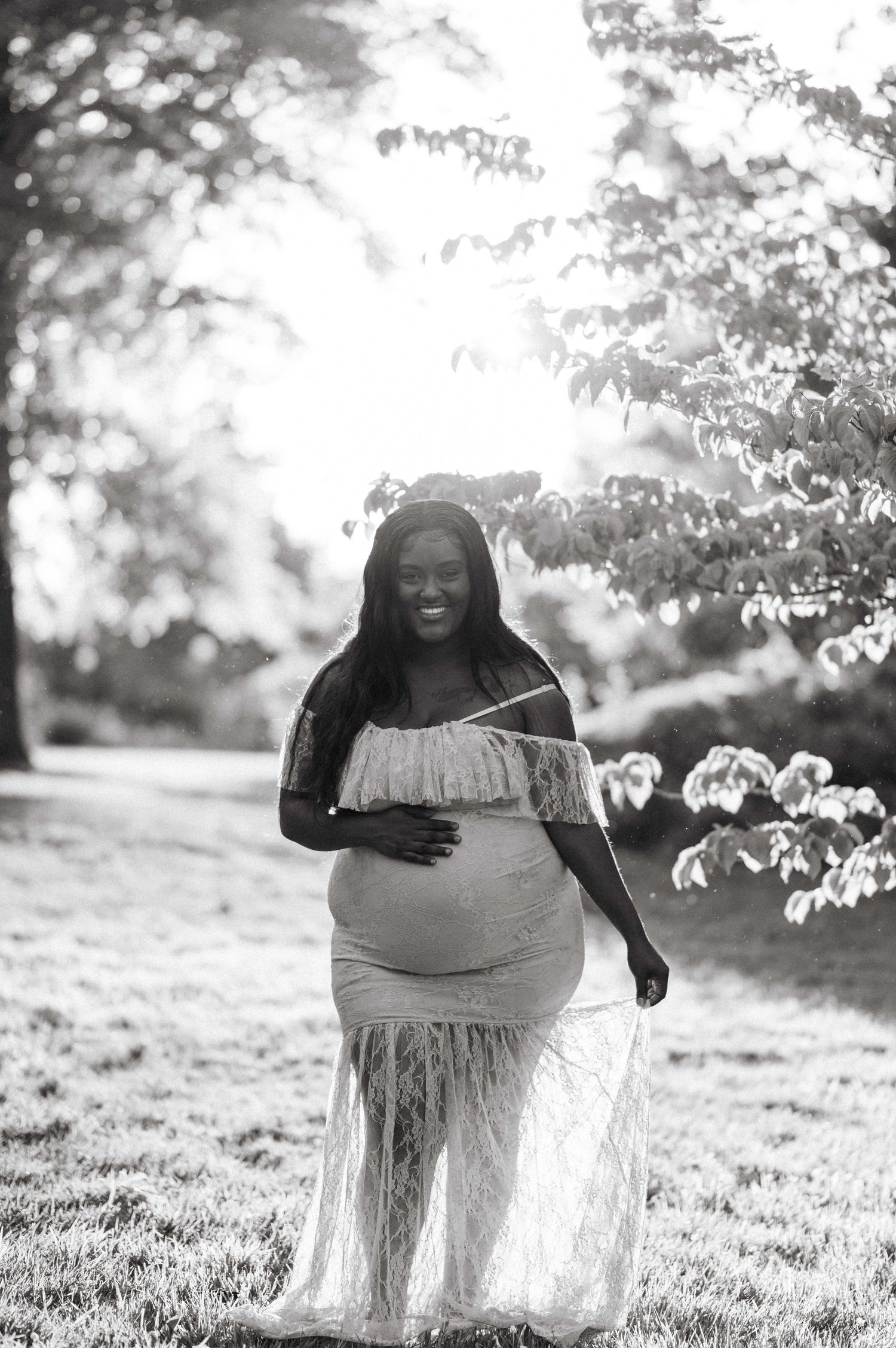 Black and white maternity photo series taken in a sun-dappled meadow with delicate lace details.