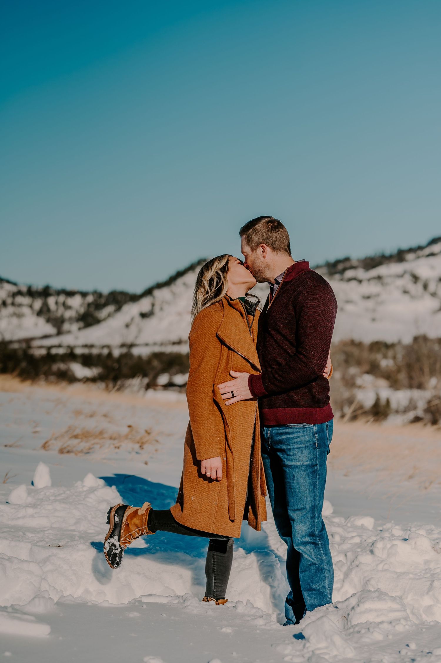 Couple shares romantic winter moments in sequence of snowy mountain engagement photos against blue sky and white snow.