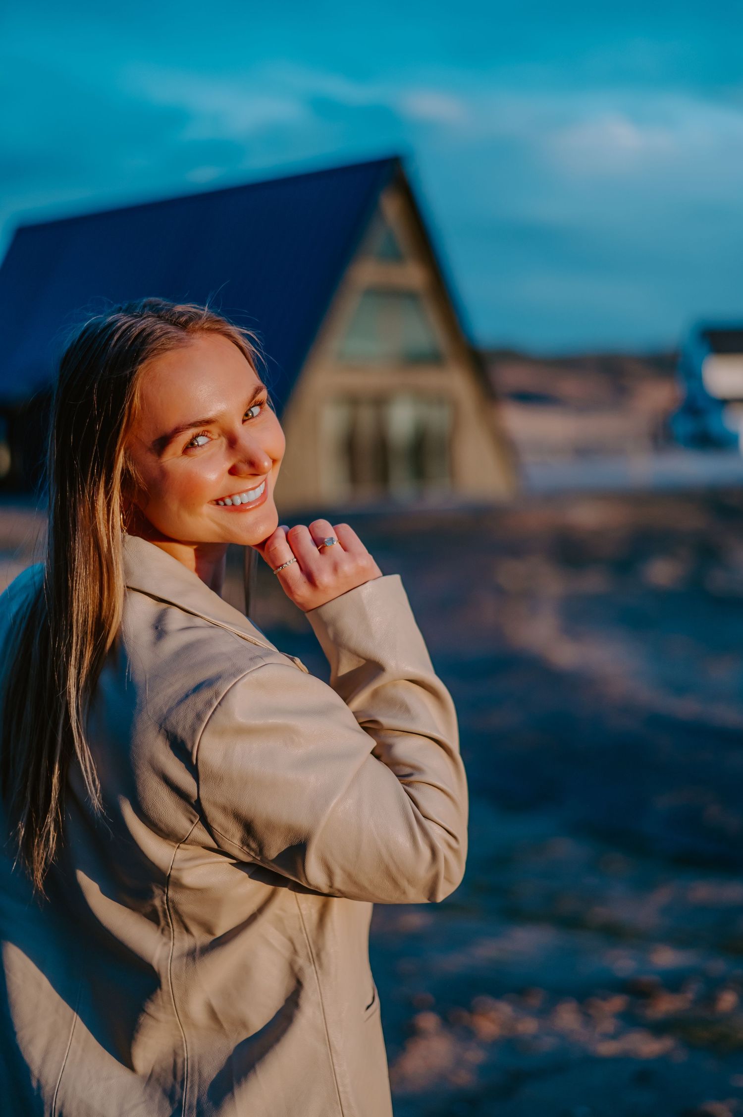 Professional portrait at sunset showing a beige blazer against an A-frame house with blue roofing in the background.