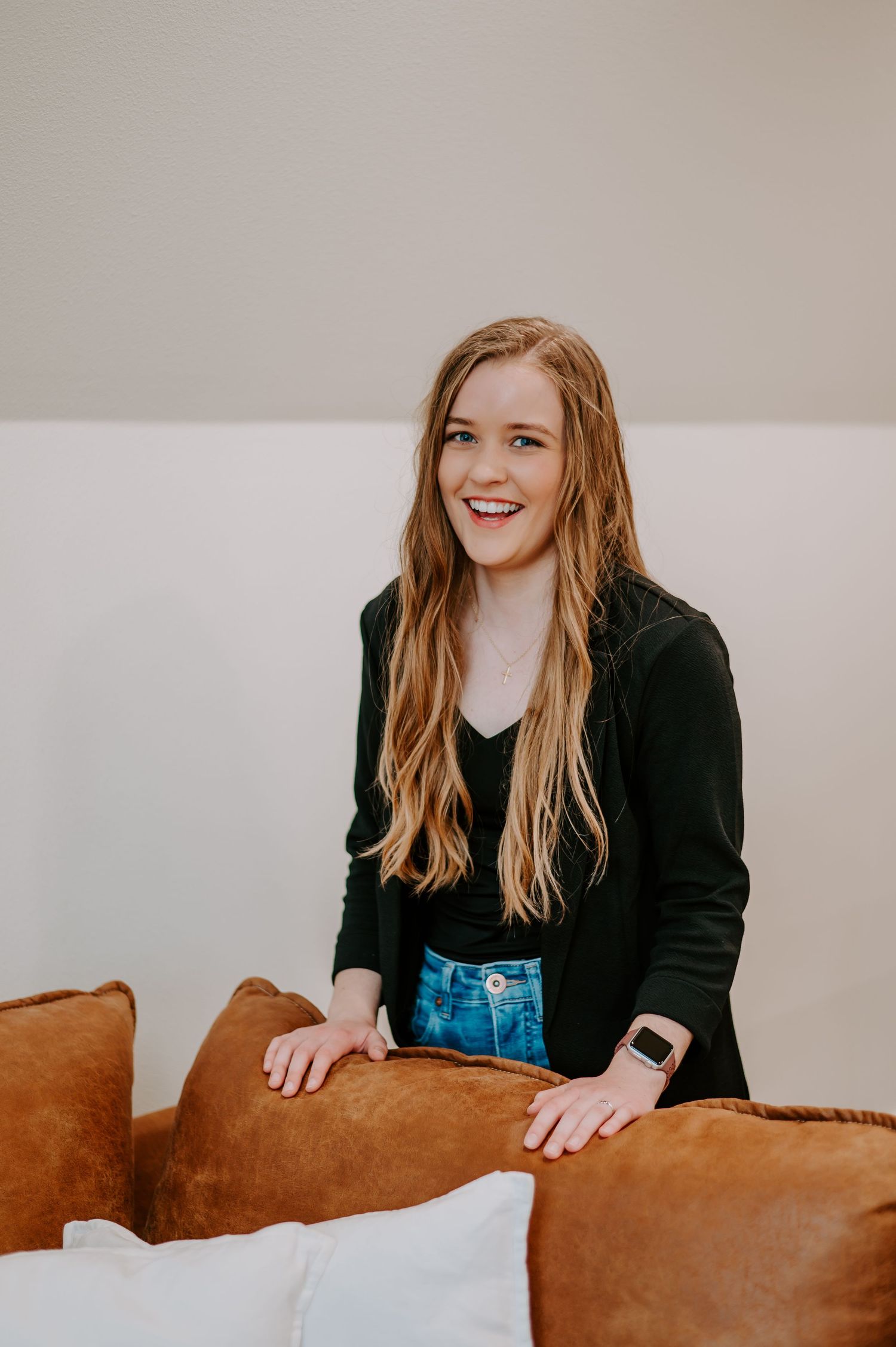 Person in casual outfit smiling while leaning on brown leather couch.