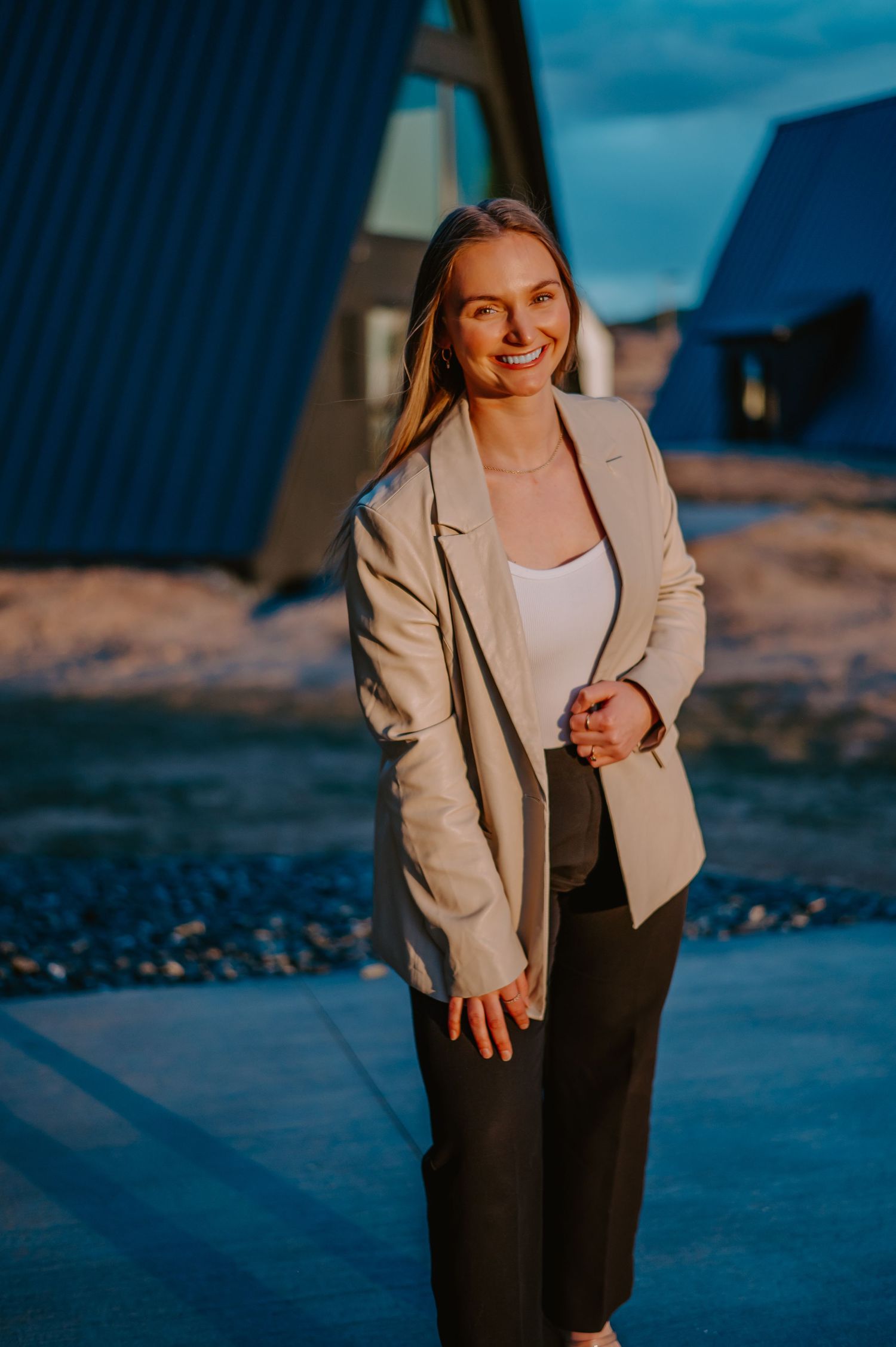 Outdoor fashion portrait featuring a beige blazer and dark pants with architectural elements in the background.