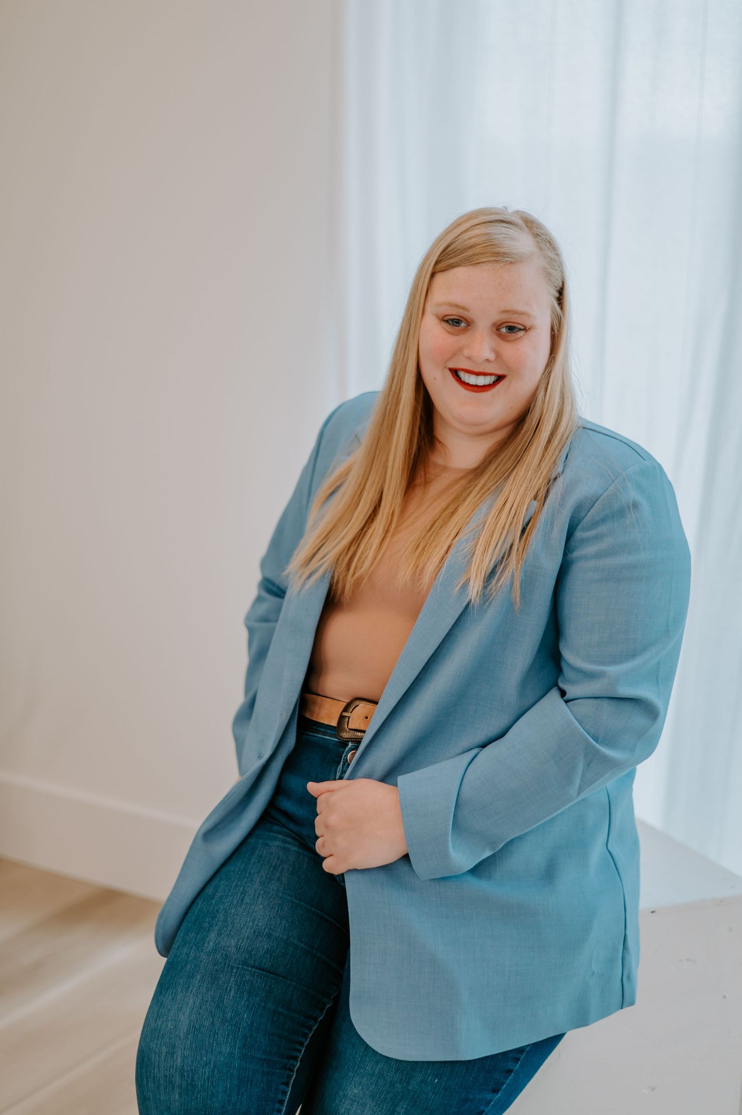 Casual indoor portrait wearing a turquoise blazer and jeans in a minimalist setting.