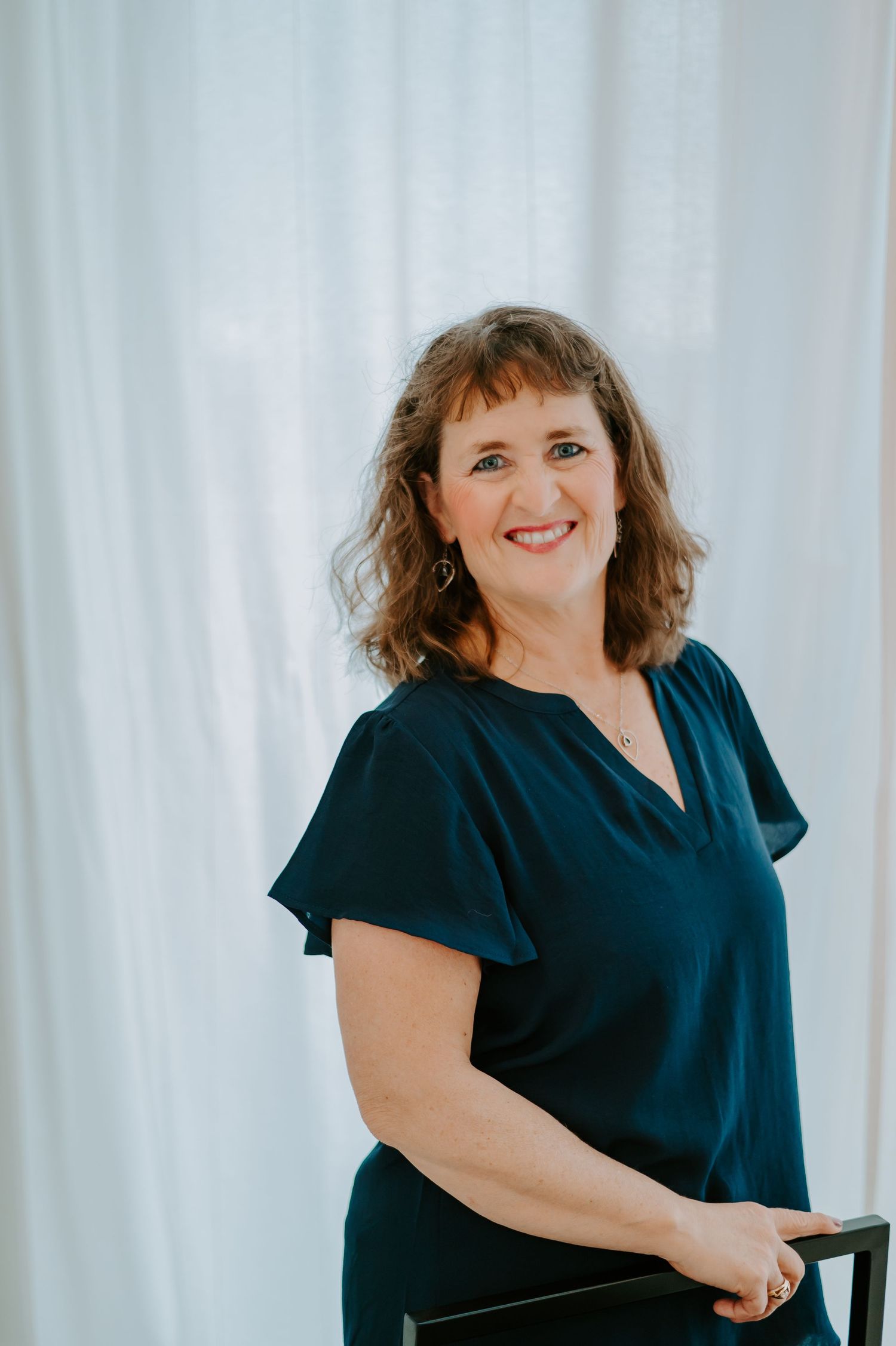 Person in navy blue v-neck blouse posing against white curtain background.