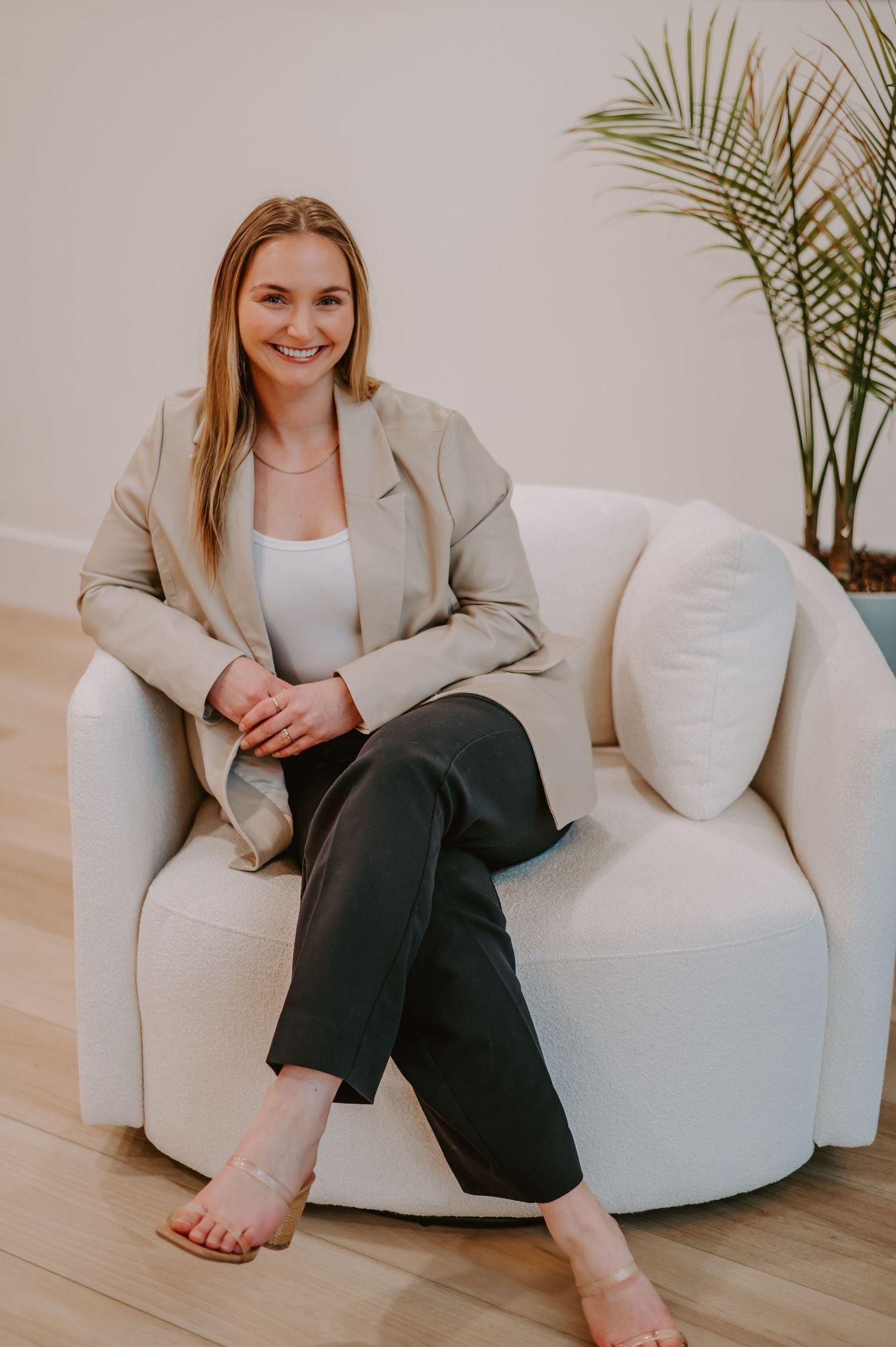Professional portraits of person lounging on white chair wearing beige blazer.