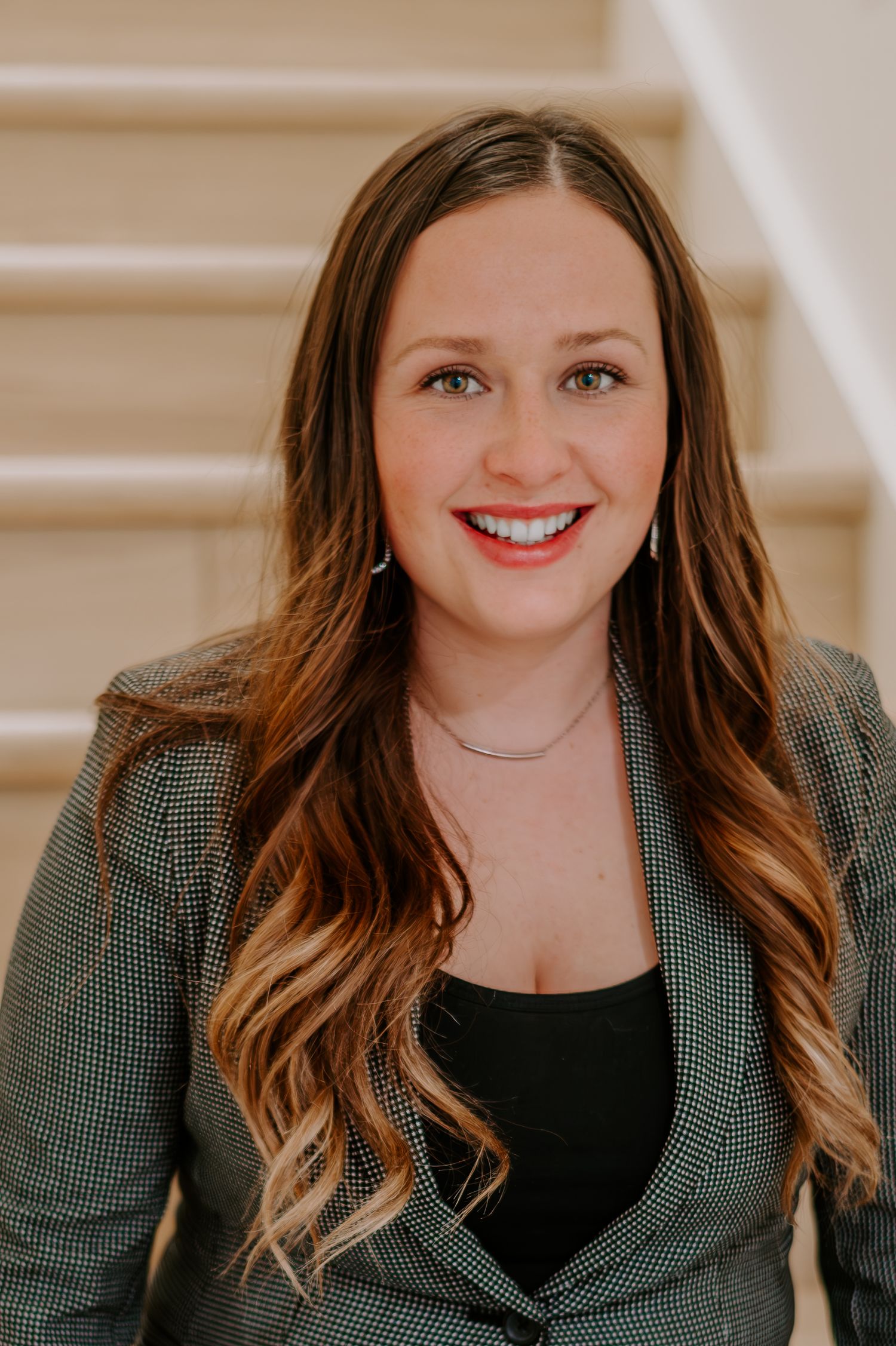 Professional headshot featuring a dark green plaid blazer and wavy hair against neutral background.