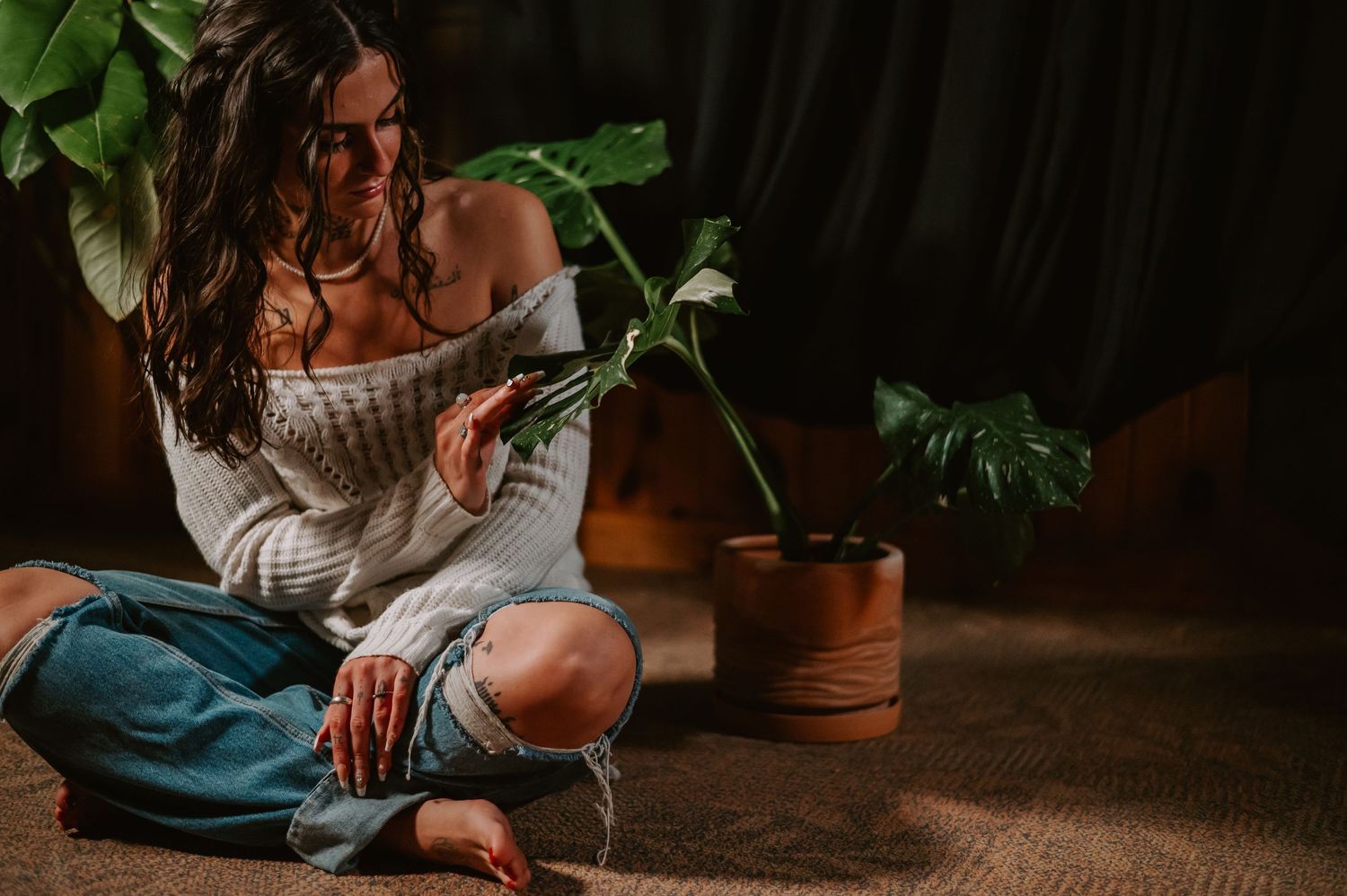 A woman waters a potted plant collection in a cozy indoor space, surrounded by greenery and warm lighting.
