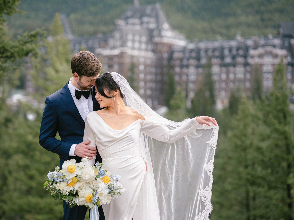 Elegant couple posing before a scenic castle surrounded by lush forest for European weddings