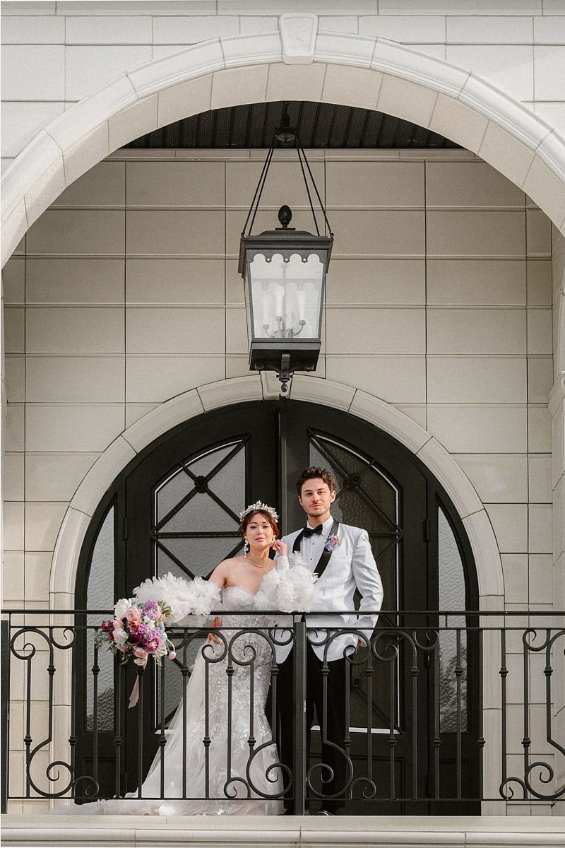 Bride and groom enjoying wedding moment from manor balcony, overlooking guests in Riga celebration