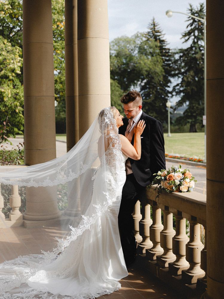 Bride and groom playing with veil by historic Riga building, romantic wedding moment