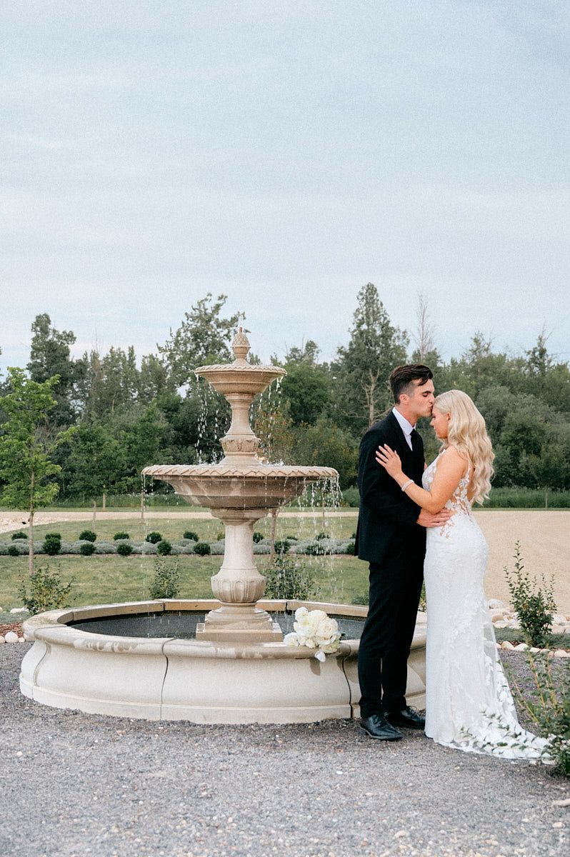 Bride and groom embracing by a Riga fountain, romantic wedding portrait in natural light