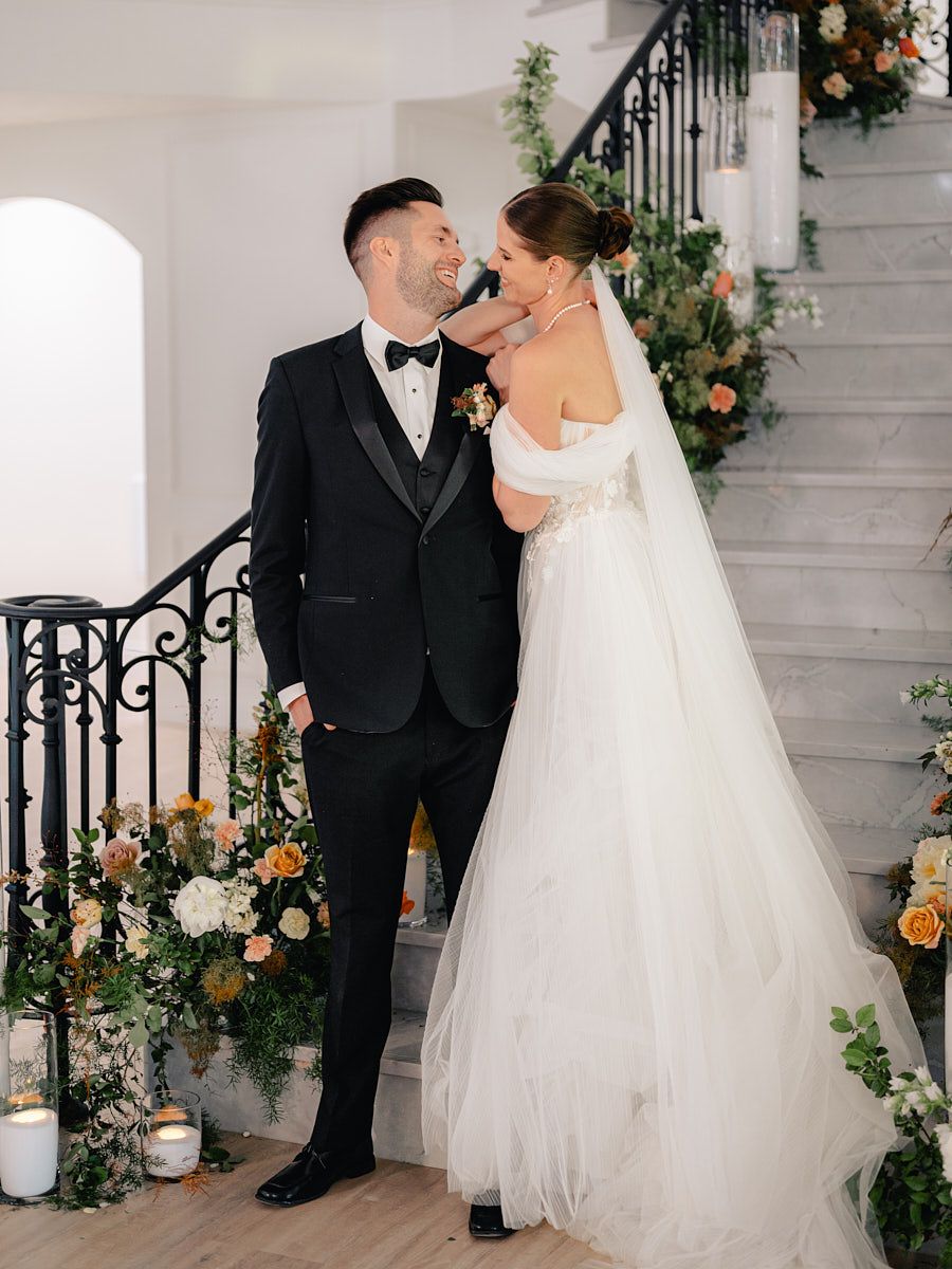 Bride and groom posing on floral-decorated stairs, romantic Riga wedding portrait