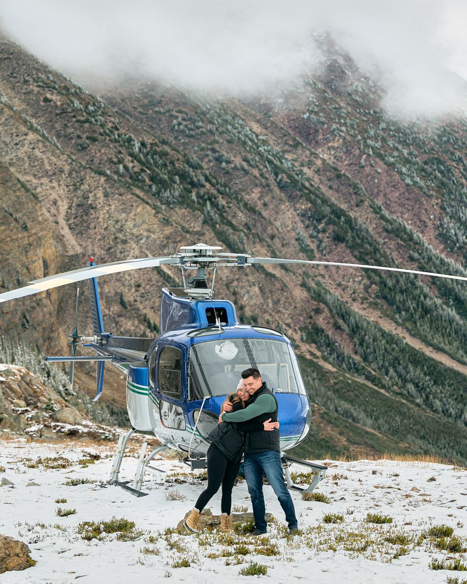 Engaged couple sharing a kiss next to helicopter, adventurous engagement session in Europe