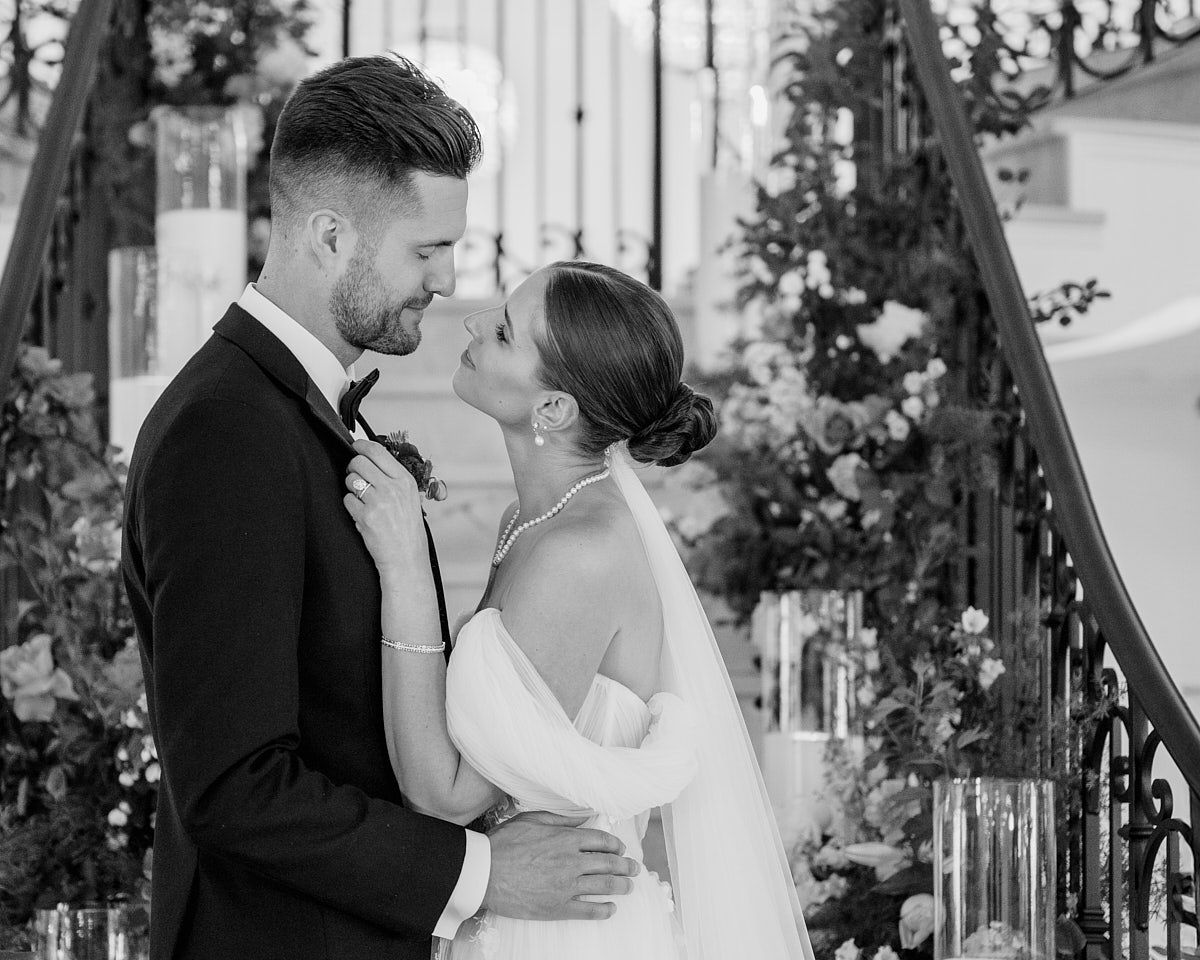 Bride lovingly adjusts groom’s bowtie, intimate Riga wedding moment with natural light and romantic connection