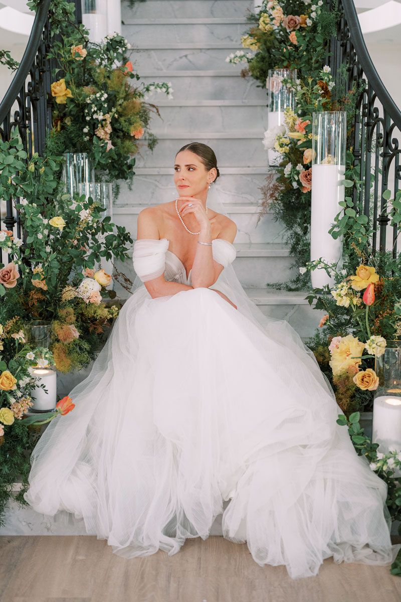 Bride posing on flower-covered stairs, romantic Riga wedding portrait with lush floral decor