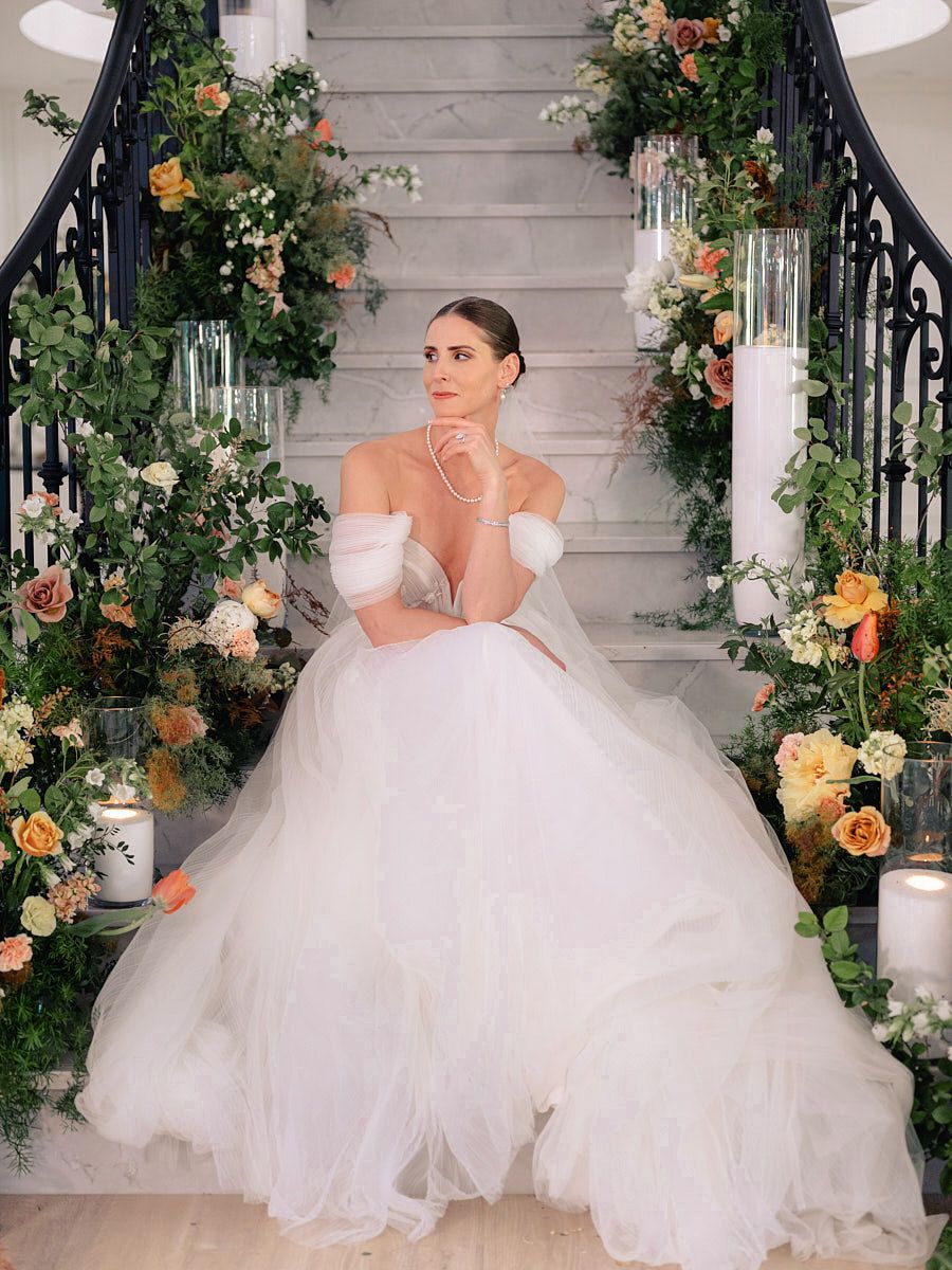 Bride seated on grand floral stairs, elegant Riga wedding portrait