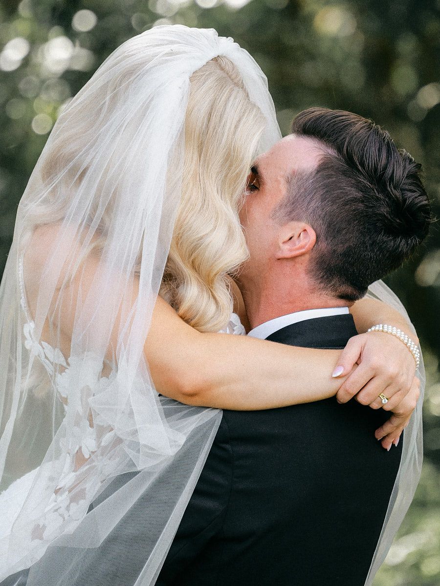 The bride and groom share an intimate embrace on the scenic grounds of Latvian wedding venue