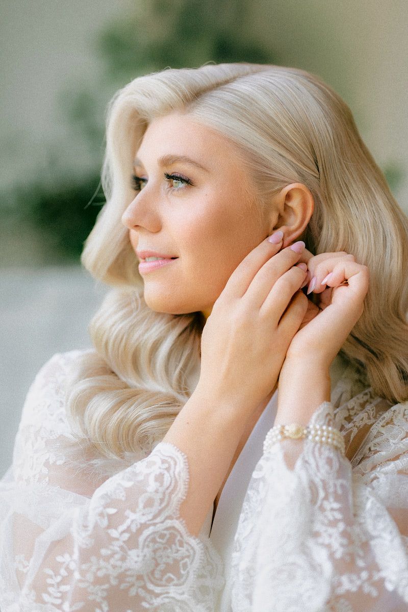 Bride getting ready in Riga, putting on earrings in a beautifully lit bridal suite.